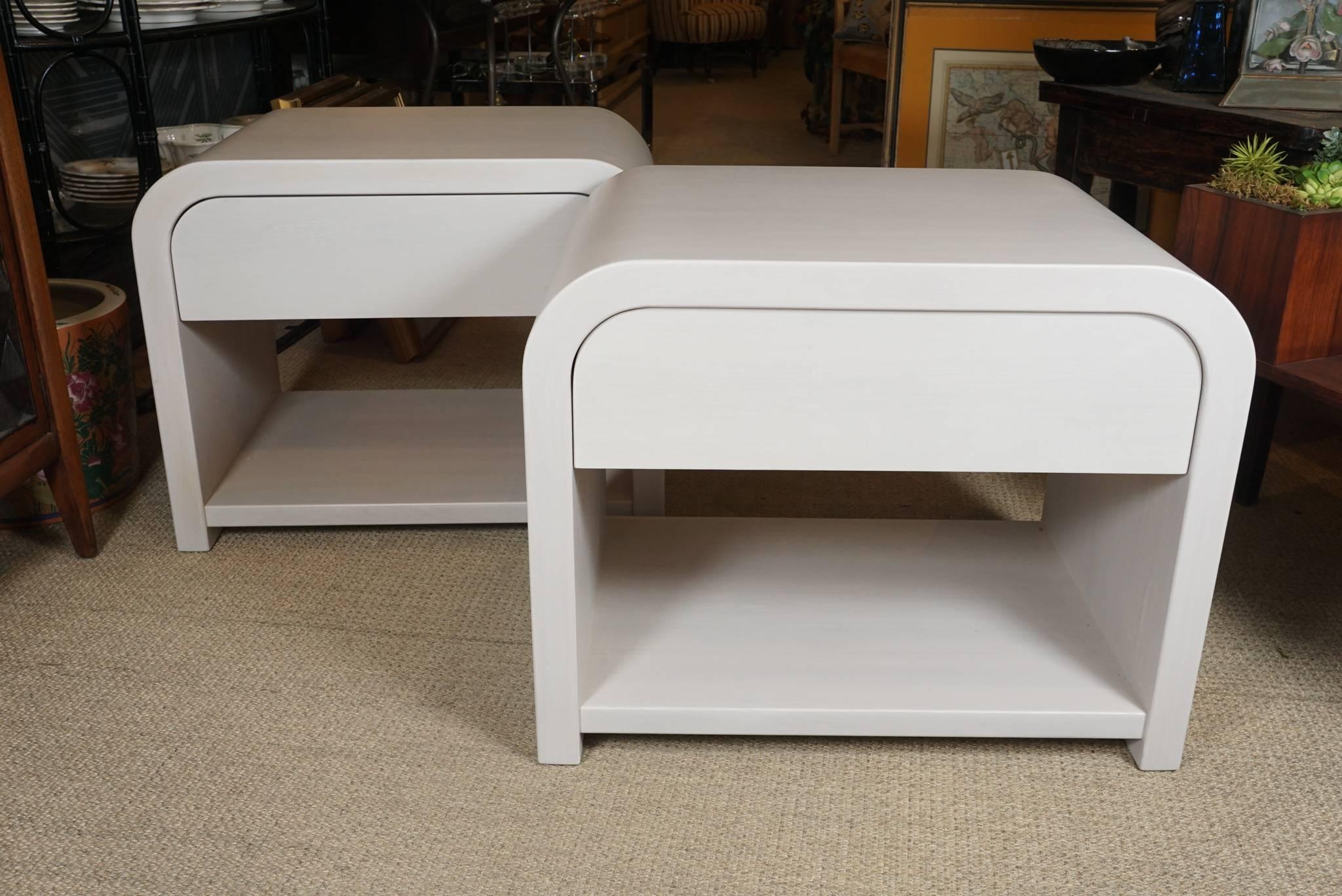 Here is a great pair of modern end tables with a waterfall edge in a cream colored white washed finish.
The wooden tables are originally from the 1970s and have a new painted finish. The tables have a single drawer with
metal runners and a bottom