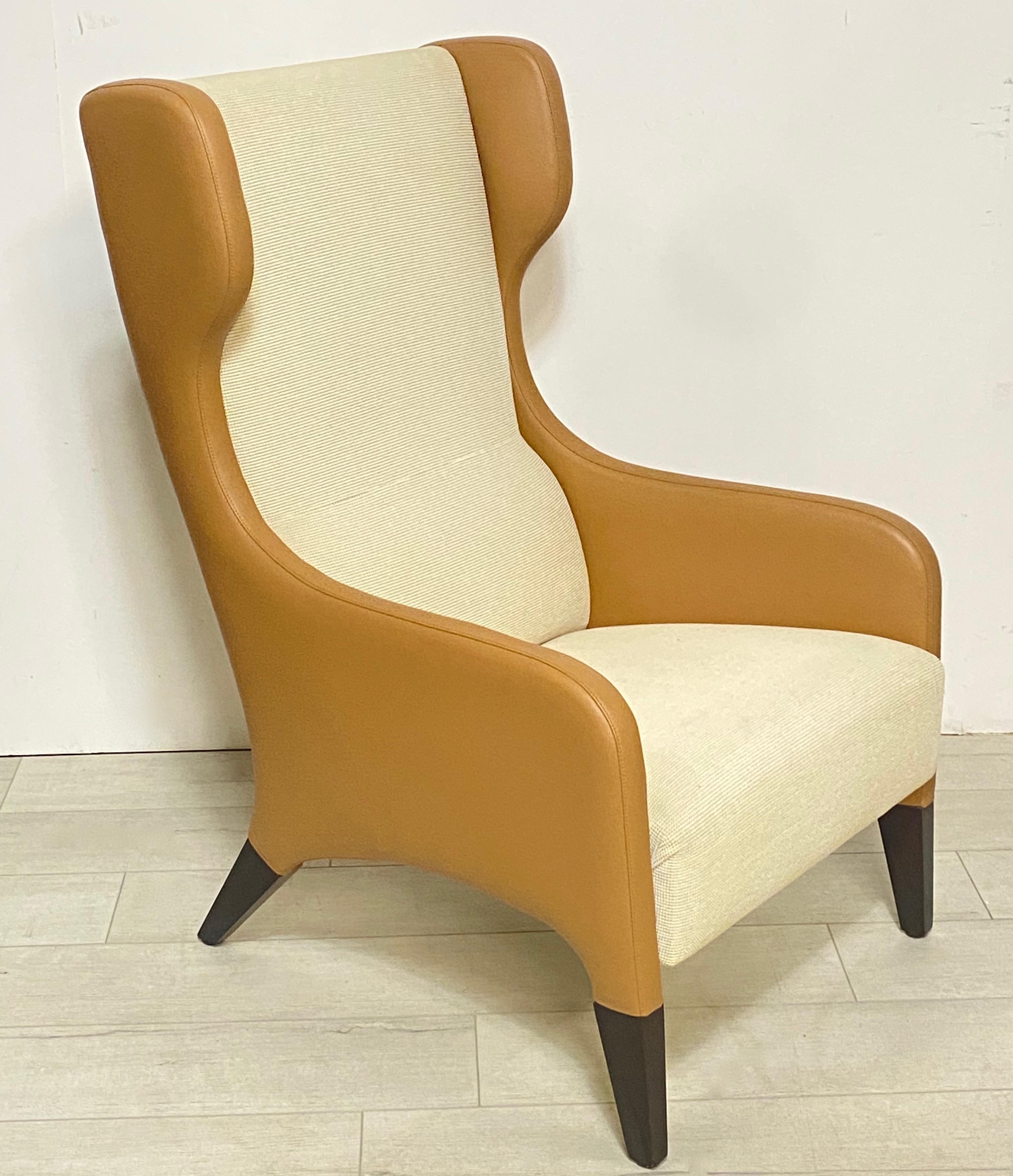 A pair of stylish and comfortable modern wingback chairs in the unique design style of Gio Ponti. Two-tone, tan leather with ivory color upholstery, and ebonized legs. 
Contemporary, late 20th century.
Measures: Height 41 inches
Width 26
