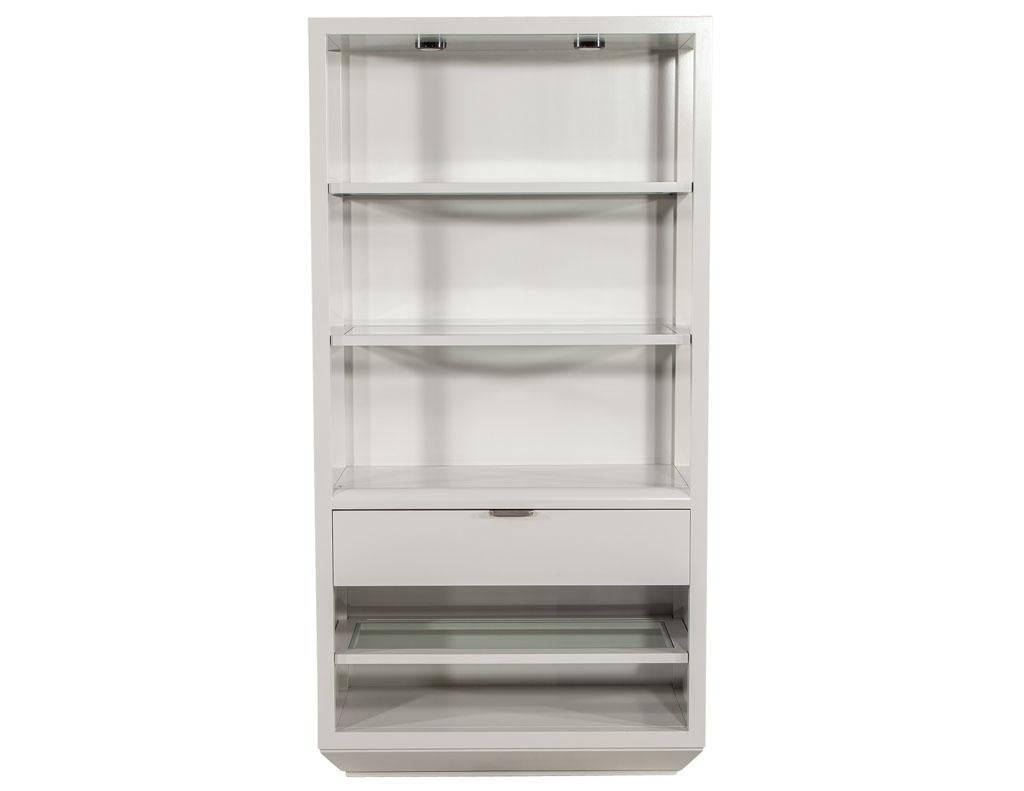 Pair of modern grey bookcase cabinets. New, made in the USA and custom finished by the Carrocel artisans. Minimalist design featuring 3 glass shelves and large storage drawer with metal handle. Cabinet lights up with 4 lights, 2 on the top of