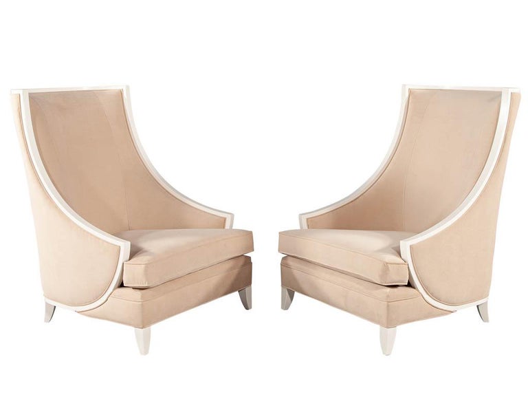 Pair of modern high back lounge chairs with designer cream velvet. Art deco inspired frames, made in Italy. Upholstered in a beige cream designer velvet and finished in a satin hand applied white lacquer. Unique curved profile and shape make these
