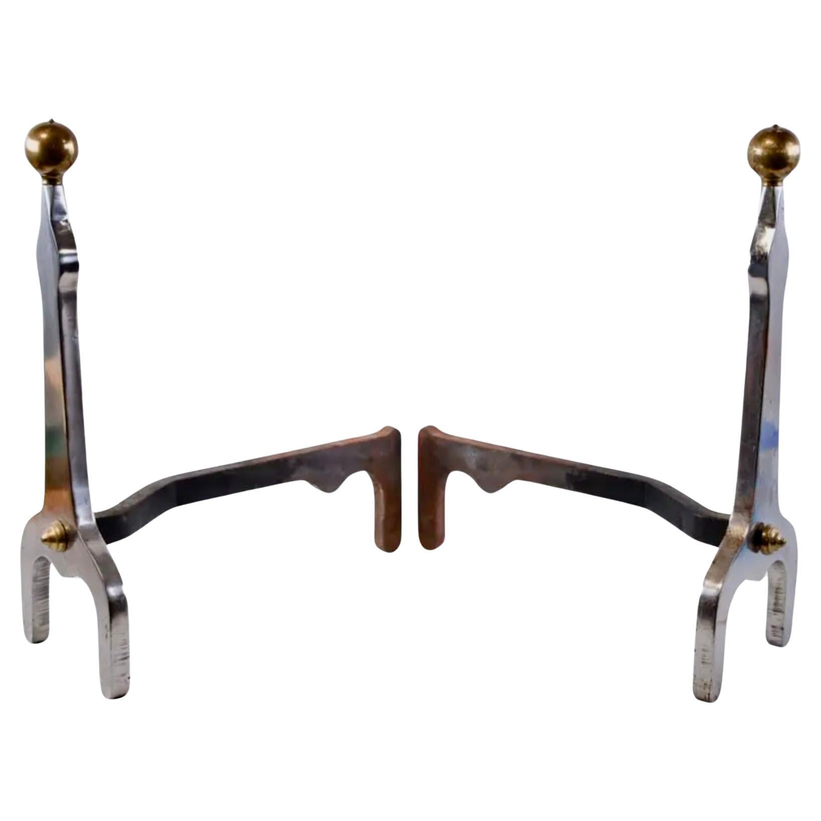 A very unusual pair of heavy polished steel andirons with brass ball tops and brass finials attaching the substantial wrought iron billet bars to the fronts. The design is spare and elegant, loosely based on English polished steel Arts and Crafts