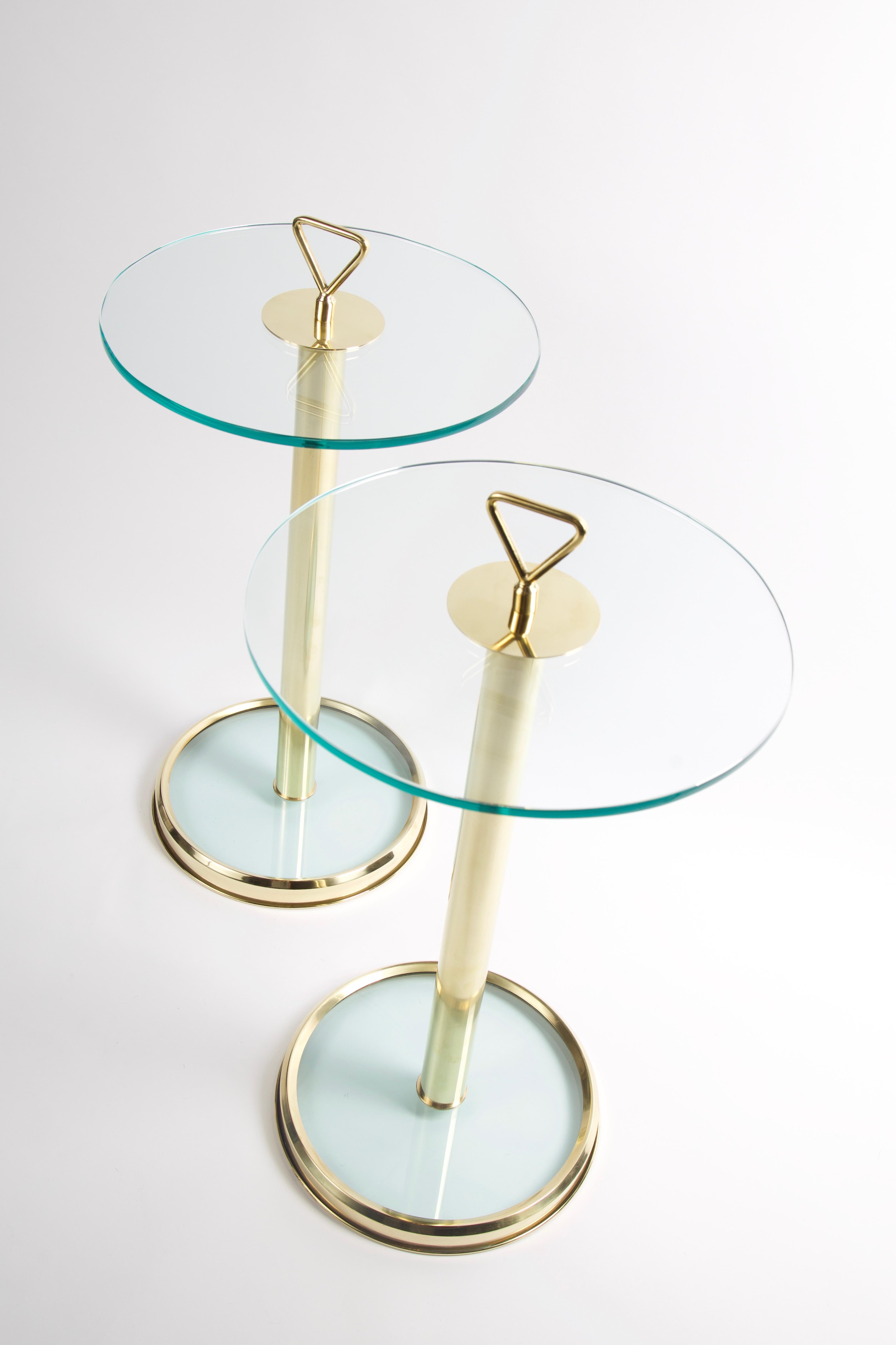 The pair of modern Italian tables features a glass top supported by a polished brass base. They are accented with a minimalistic triangular handle on the top. The glass base of the tables are incased in a beveled brass frame with a 12.5 inch