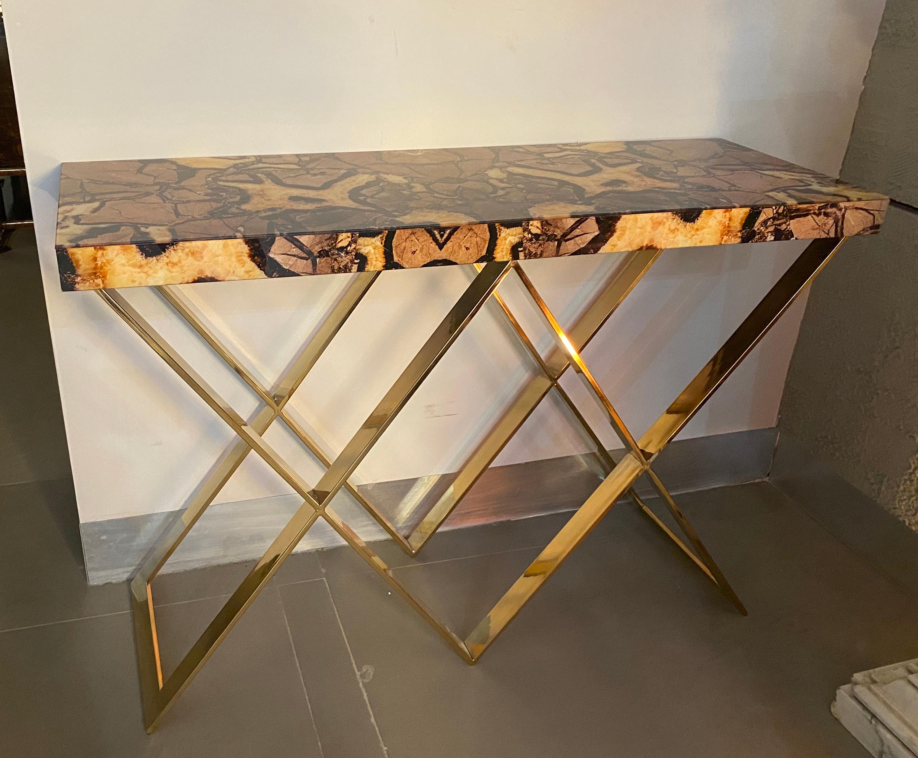Exceptional console Tables with double X-shaped brass base .
The glass tops of these pair of consoles are made with the imitation of a semi-precious stone called “septaria”, which is formed by overlapping mineral deposits and is crossed by crystal