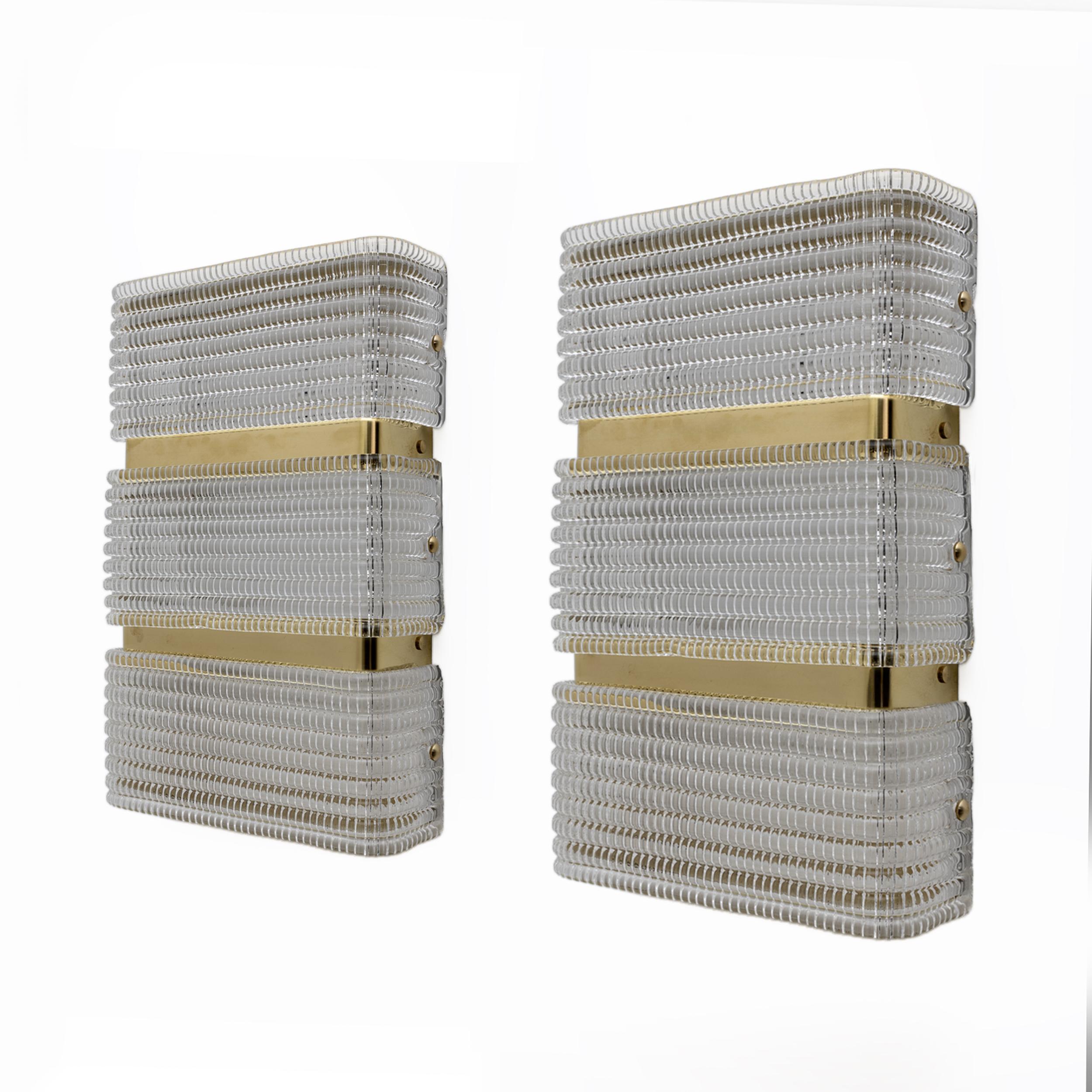 This pair of wall lamps features three glasses and a metal and brass structure; blown and pressed glass to obtain a textured effect, translucent and structured crystal-colored Murano glass. Overall, the lamps have an elegant and contemporary