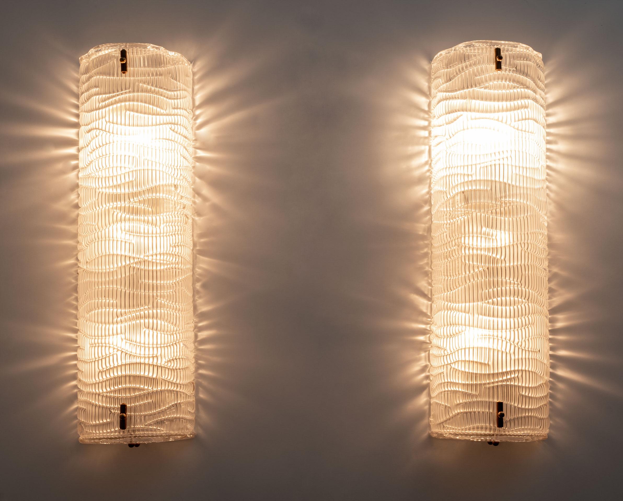 Pair of wall lamps in structured Murano glass. The glass is textured with ribs and has a curved design, creating a superb decorative impact, completely enclosed by glass plates, above and below. Each wall light requires three medium base bulbs and