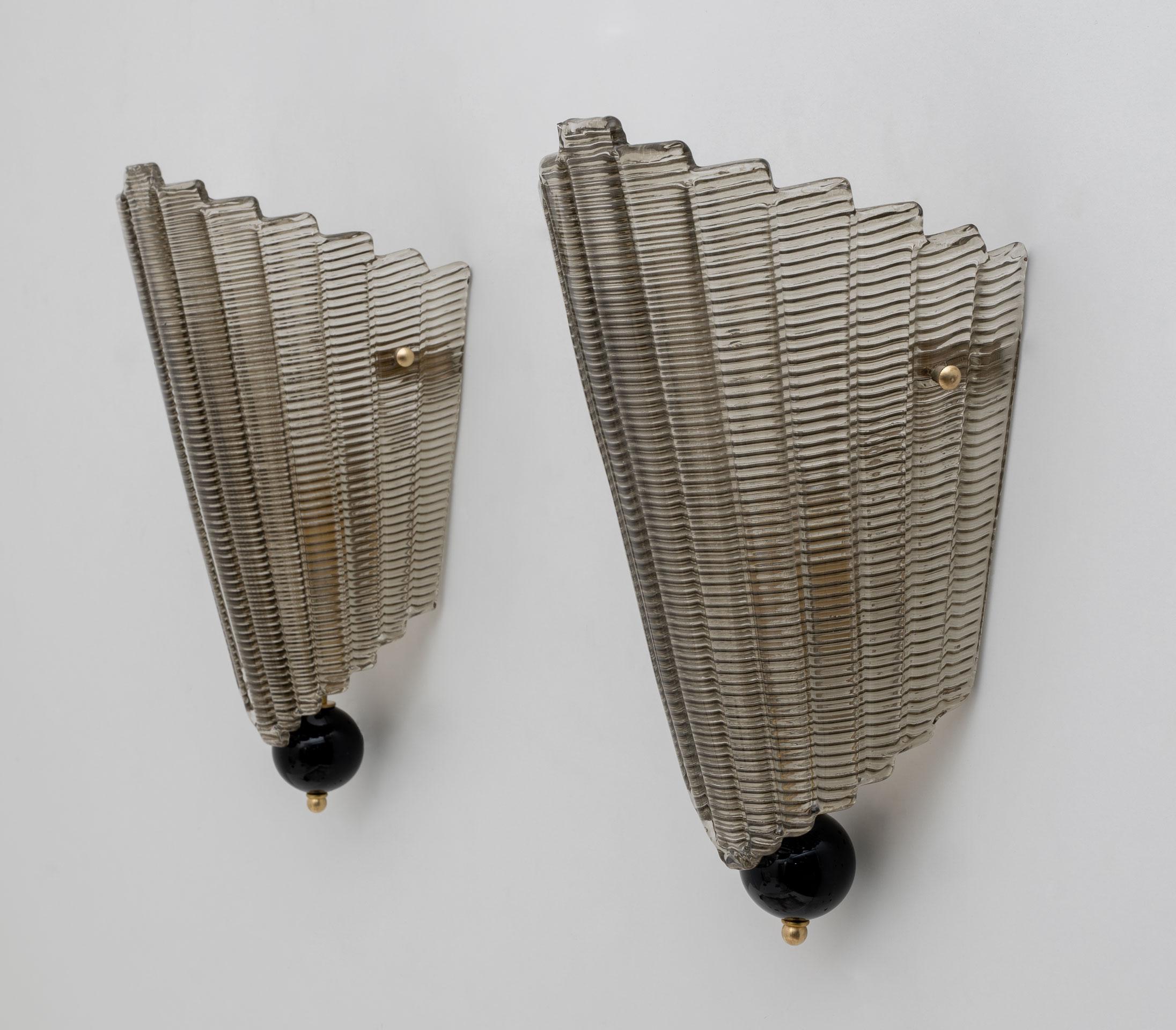 Pair of wall lamps in structured Murano glass. The glass is ribbed and has a curved design, creating a superb decorative impact, completely enclosed by a glass plate and a glass ball finial, in the Art Deco style. Each wall light requires a medium