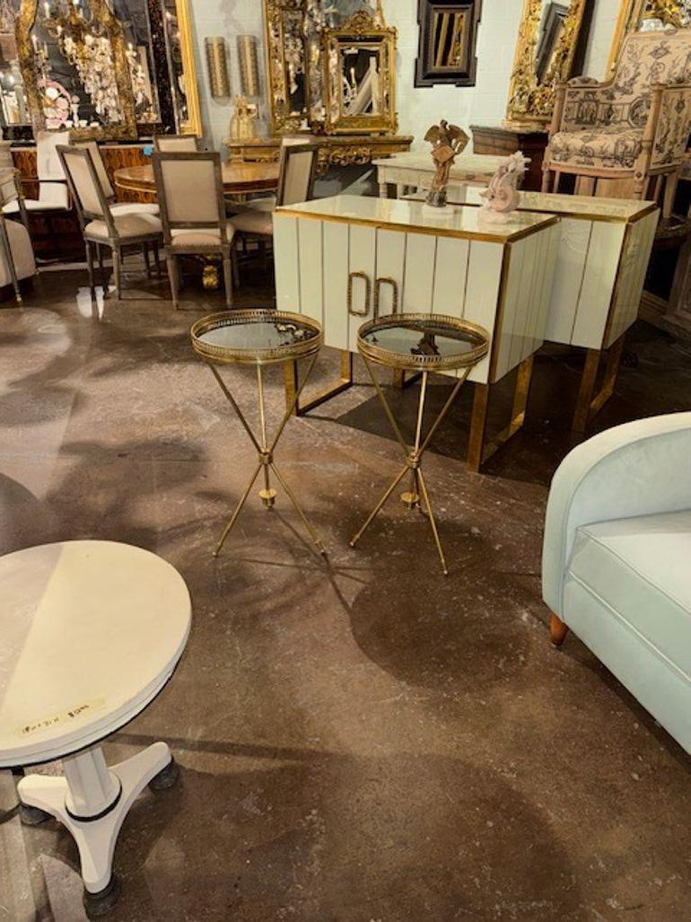 Pair of modern Jansen style brass and glass drink tables featuring a sleek and contemporary design. The tabletop material is glass, complemented by a brass finish. These tables would be a stylish and practical addition to any living space and add a