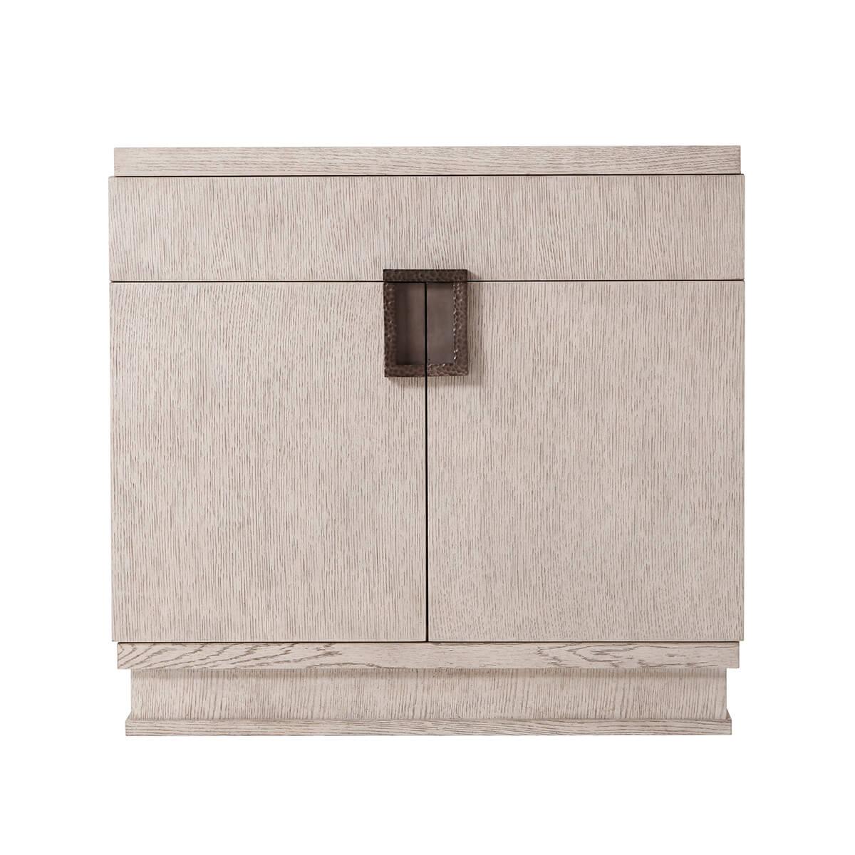 With a quartered oak veneer in the Gowan finish. With a rectangular top above a frieze drawer and two cabinet doors. With a modern brass finish handle with a hammered design. 
Dimensions: 30