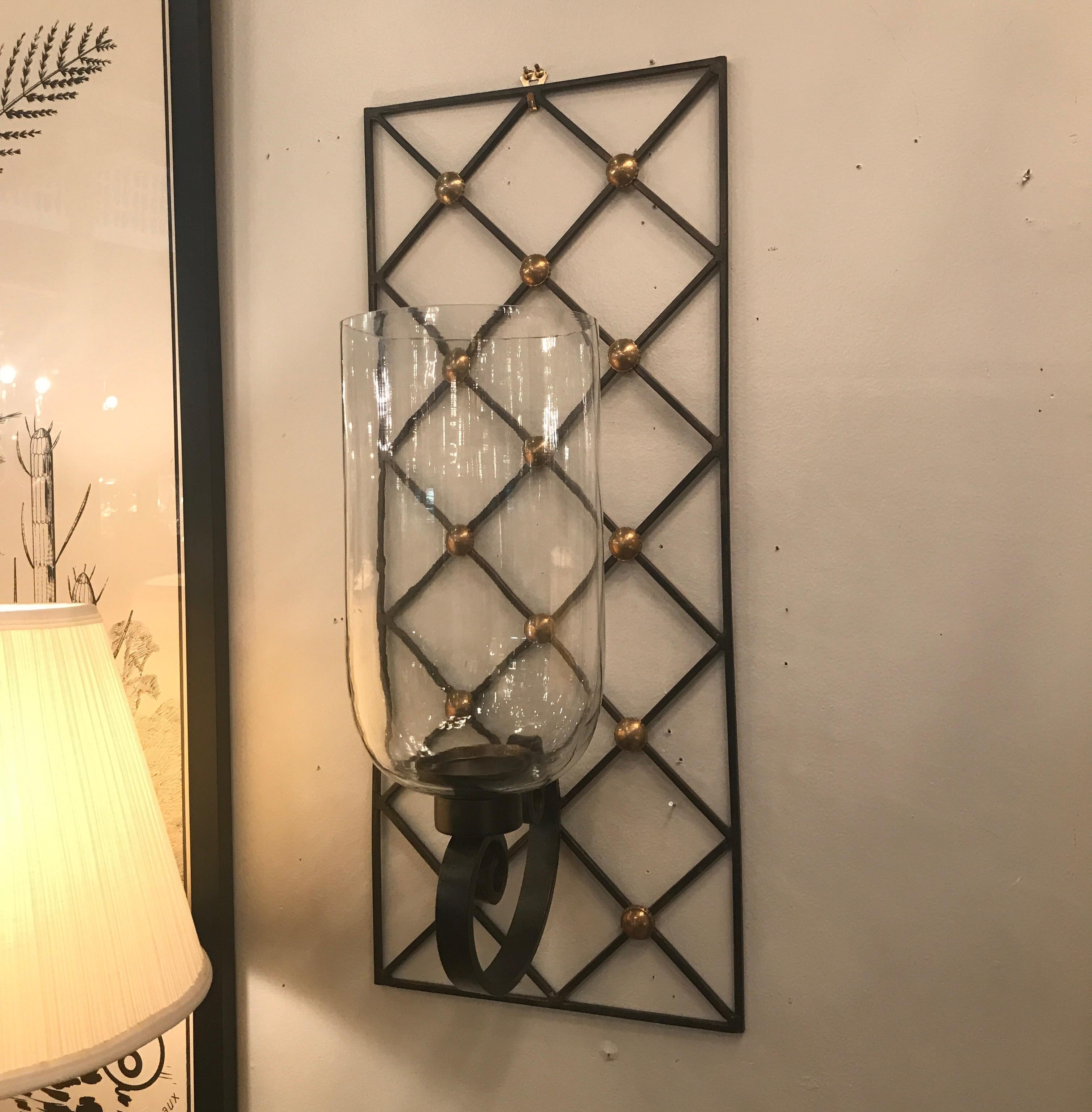 A pair of Iron, glass and brass wall sconces with hurricane shades in the manner of Jean Royère. The lattice backs with brass details and blown glass hurricane shades in a large-scale. These are candles sconces and can be used to enhance any room.