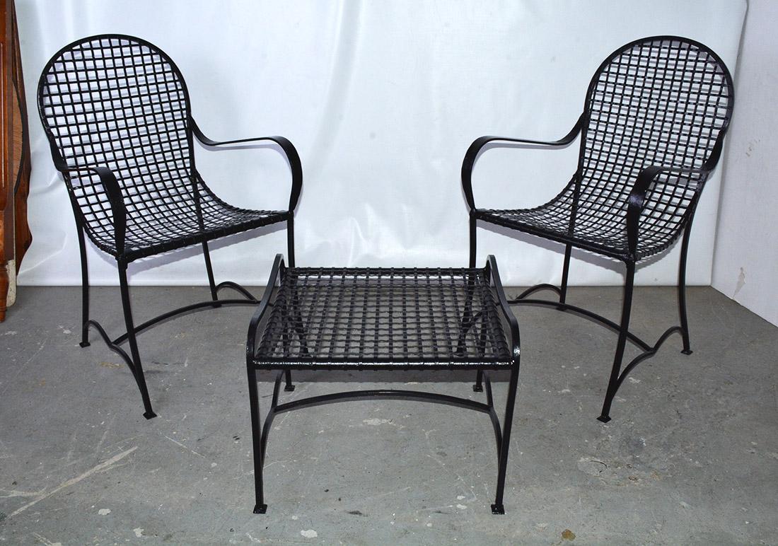 La paire de chaises longues d'extérieur et la table basse, faites de bandes de fer forgé noir à tissage ouvert. Des brancards décorativement incurvés fixent les pieds incurvés de toutes les pièces. La courbe du dossier vers l'assise ajoute au