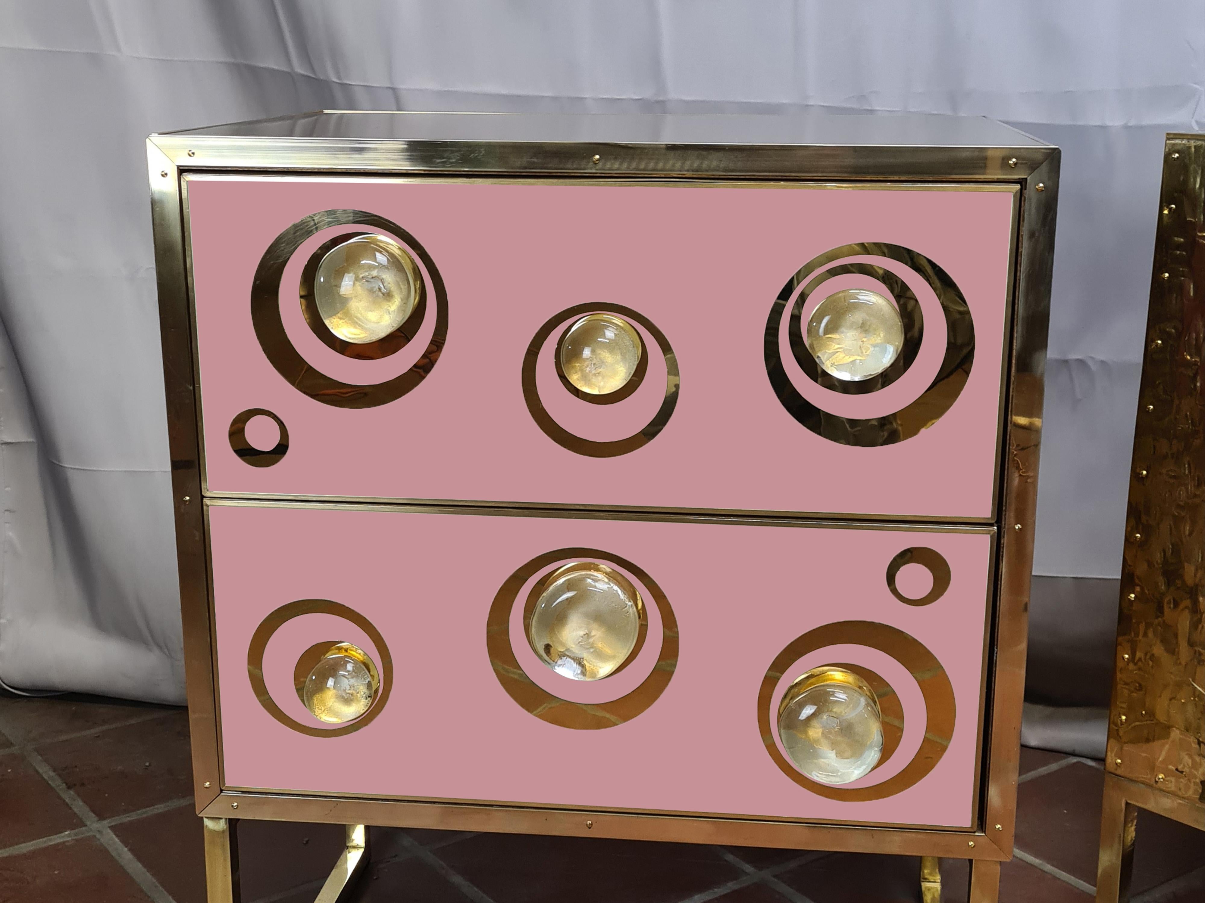 Pareja de mesillas de noche modernas de color rosa, una obra maestra de la artesanía italiana que combina la elegancia del cristal de Murano con la calidez del latón. 

Estas mesillas de noche presentan preciosos cajones rosas adornados con esferas