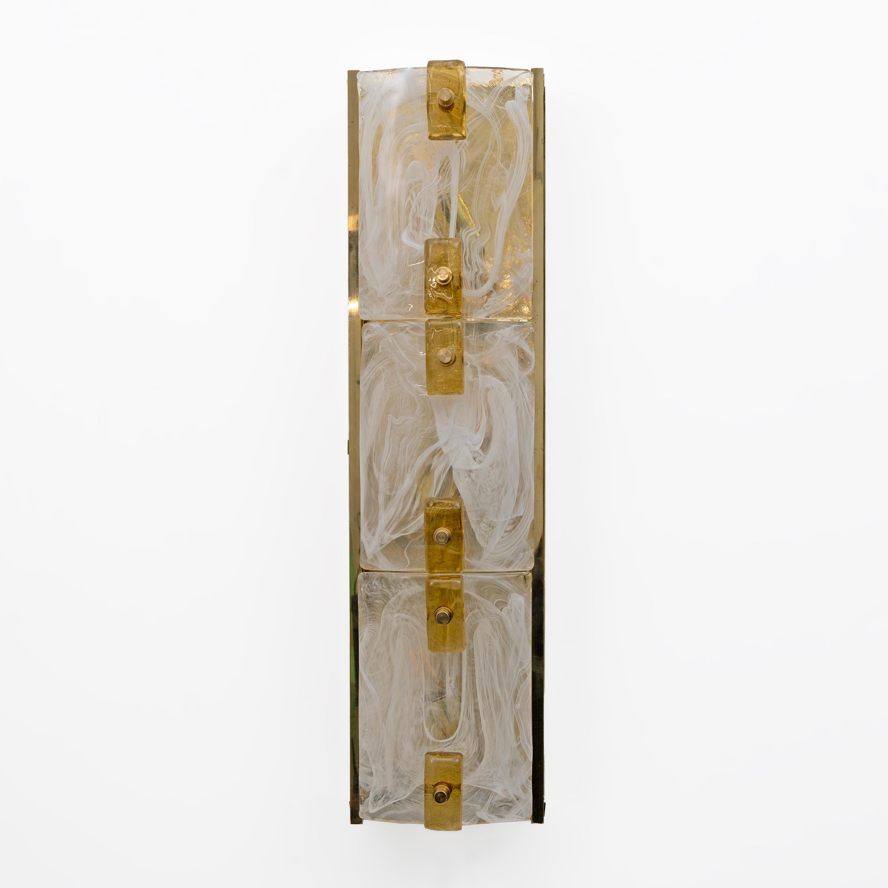 Pareja de apliques con un diseño sofisticado y elegante, caracterizado por un panel vertical compuesto por tres secciones de cristal de leche curvado, dispuestas de forma lineal y fijadas a la estructura con pasadores de latón y cubos de cristal