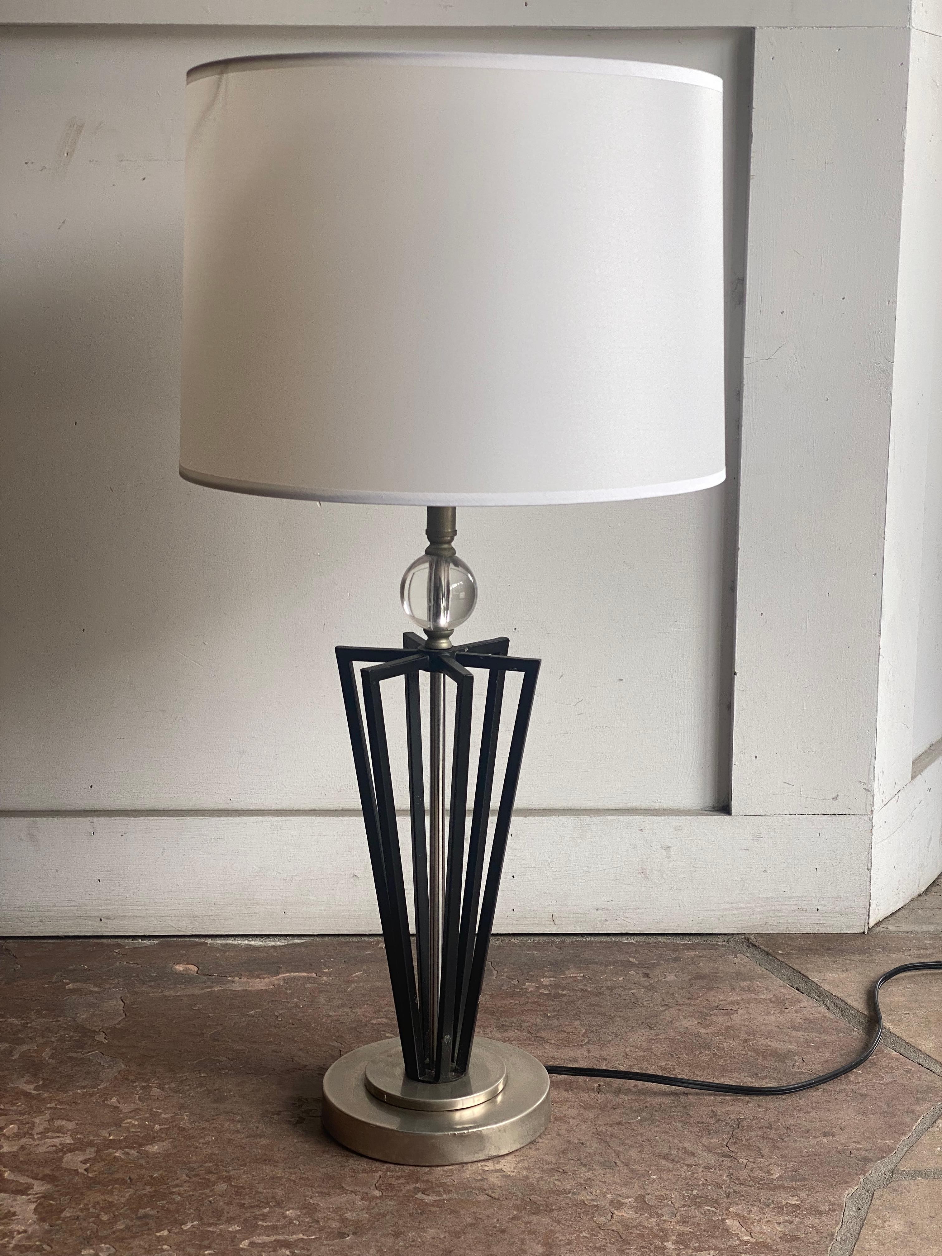 This pair of table lamps features a black metal base with a geometric, flared design resting on a circular brushed metal footing. A clear glass sphere is positioned beneath the socket, adding a subtle decorative element. Each lamp is topped with a