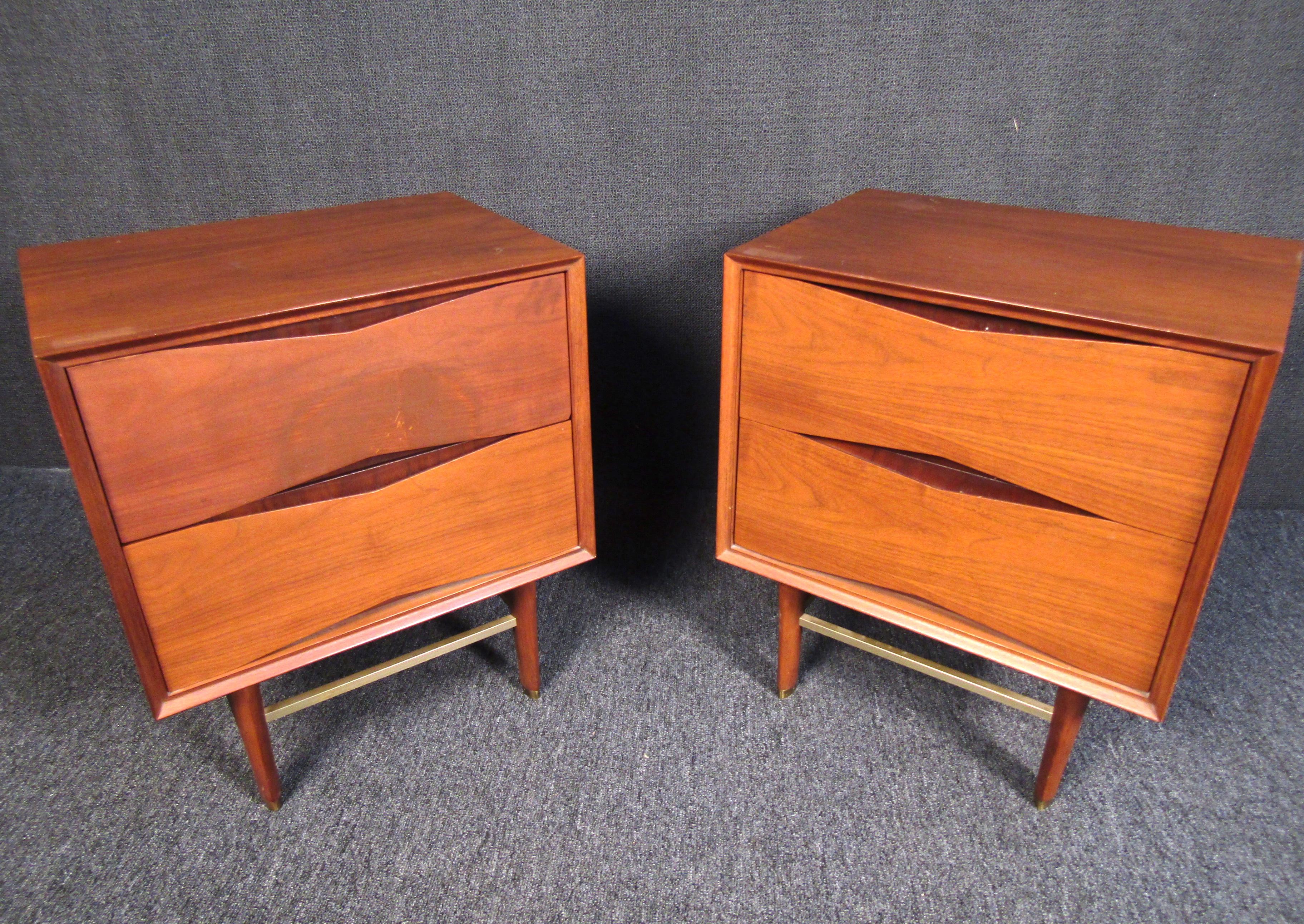 A beautiful and minimal pair of Mid-Century Modern walnut nightstands with brass accents. Perfect for adding midcentury flair to any bedroom, this pair of nightstands features an understated design with tapered legs and brilliant brass accents that