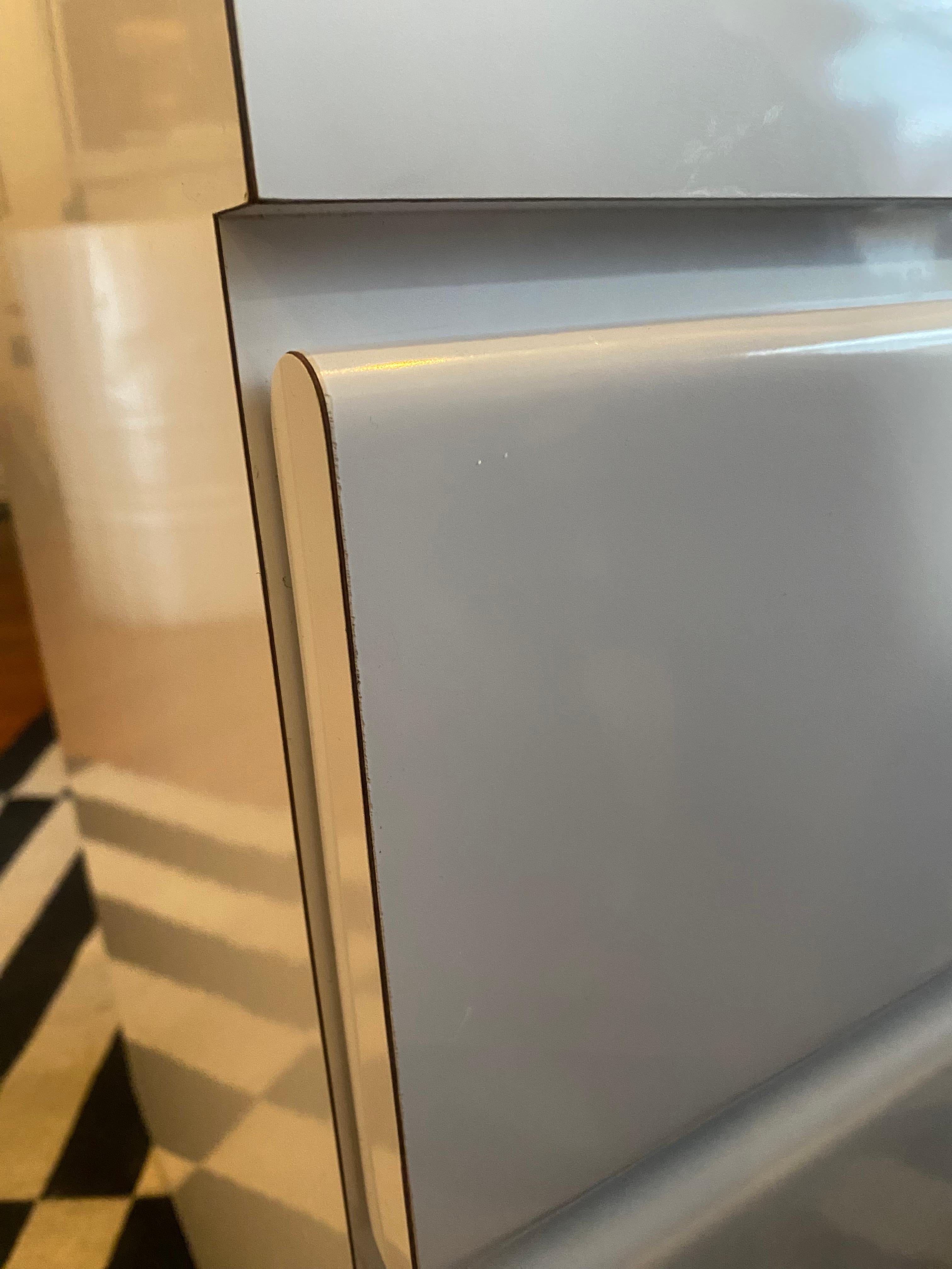 Dieser postmoderne Nachttisch aus weißem Hochglanzlaminat (um 1980) zeichnet sich durch ein elegantes Design mit Wasserfallfront und zwei Schubladen auf glatten Metallgleitern mit Arretierung aus. Seine minimalistische Ästhetik und seine kühne, aber