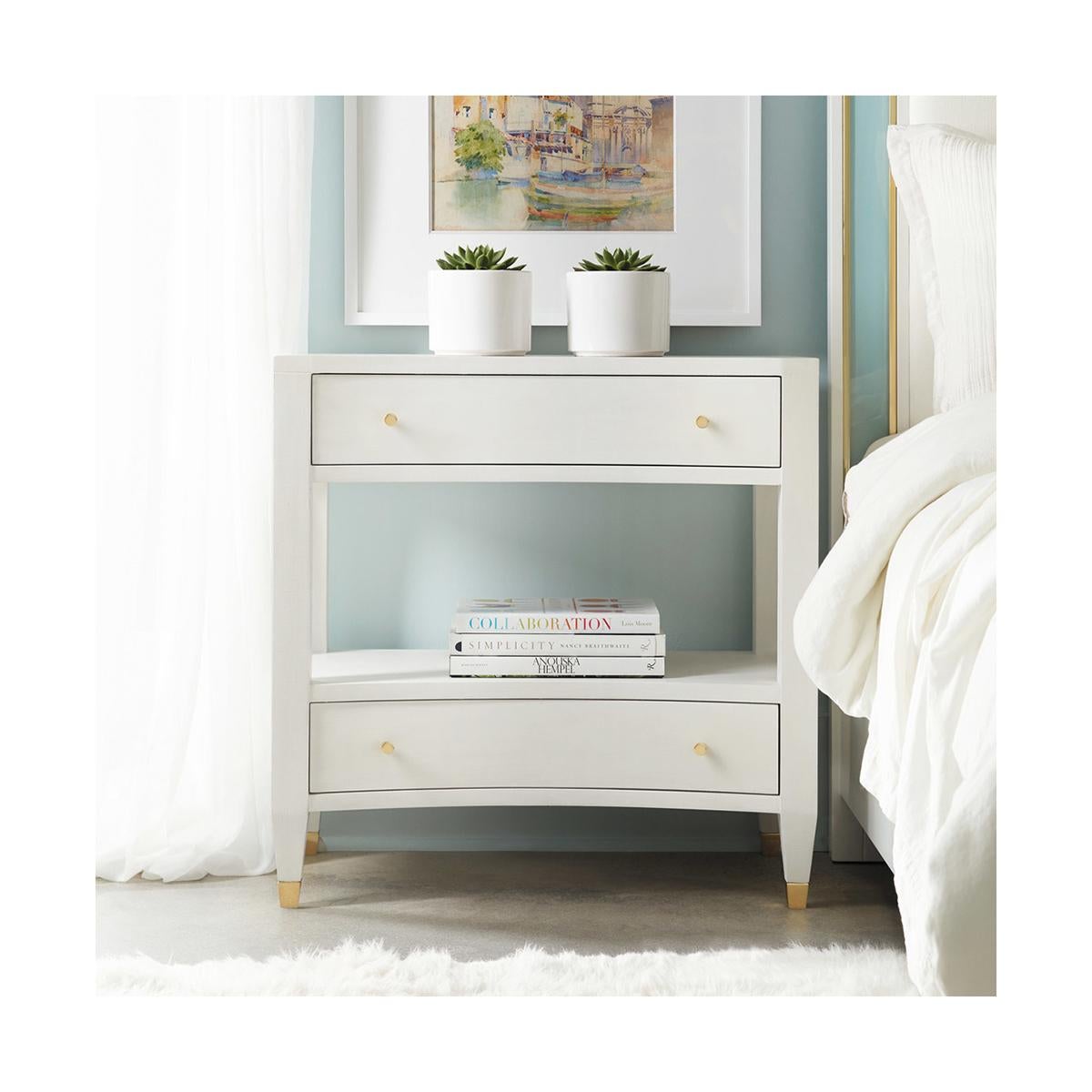 Modern White Painted Nightstand, hand painted with a white linen color, with a concave form front with two drawers and an open shelf space. Each drawer with polished brass knobs and with square tapered legs on brass feet.

Dimensions: 30