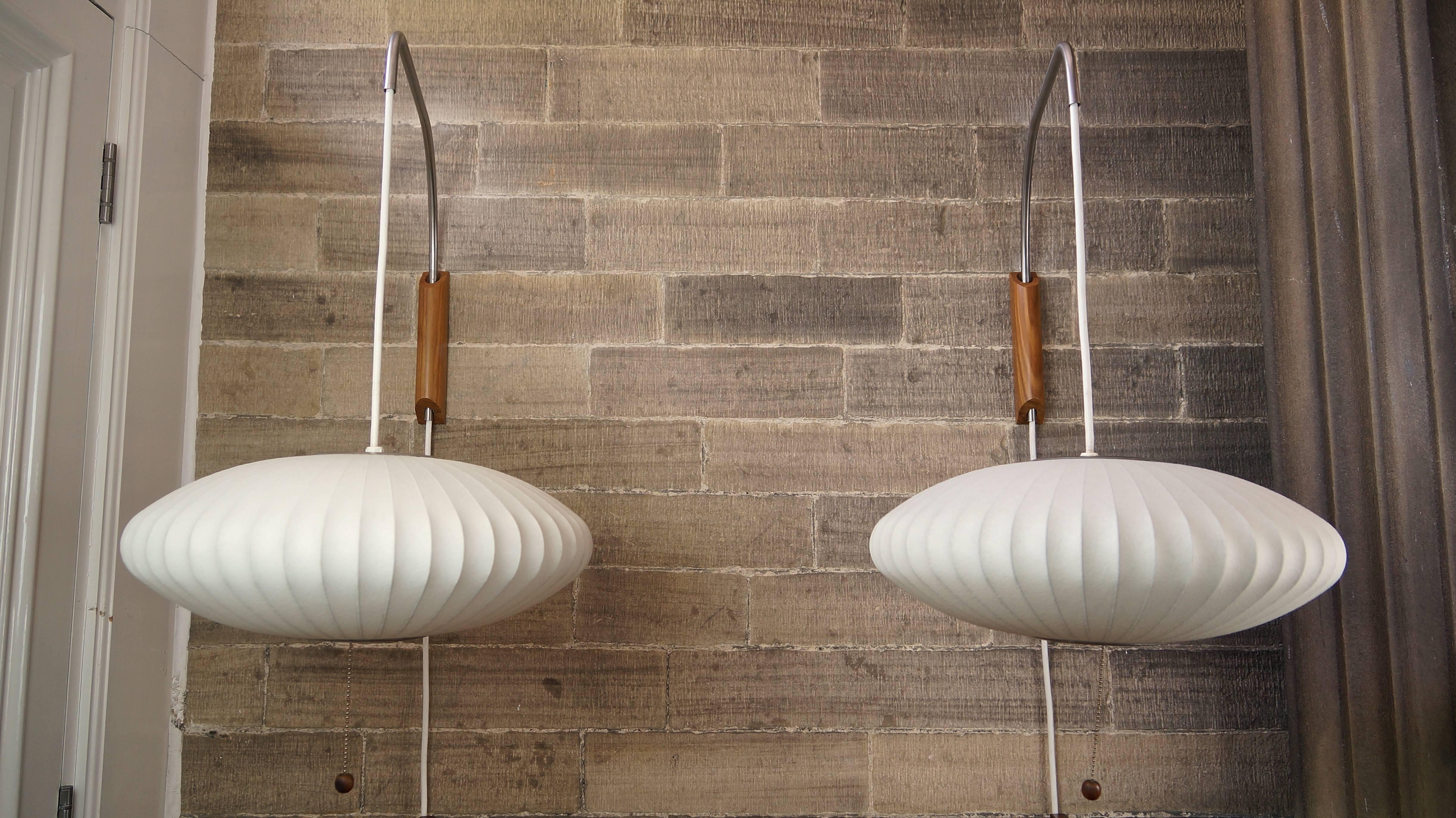 A beautiful pair of George Nelson Bubble wall lamps in the Saucer shape with walnut wall mounts. 

The iconic design allows for height adjustment of the lamp and movement of the arm from side to side to allow for the ideal positioning and the long