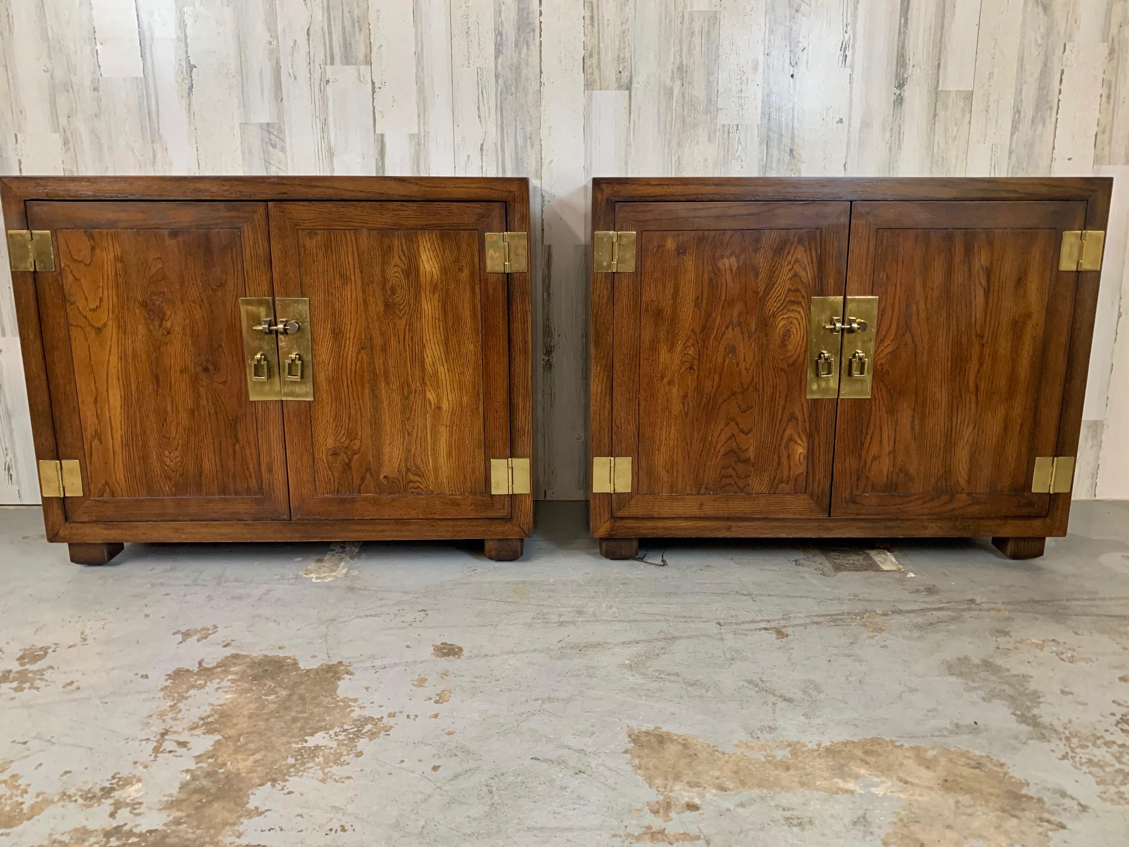 A pair of console cabinets from Henredon's Artefacts Collection, designed in a campaign style. Crafted from oak with a subtly distressed finish, it showcases banded door fronts, a sleek surface top, brass hardware, and sturdy block feet.