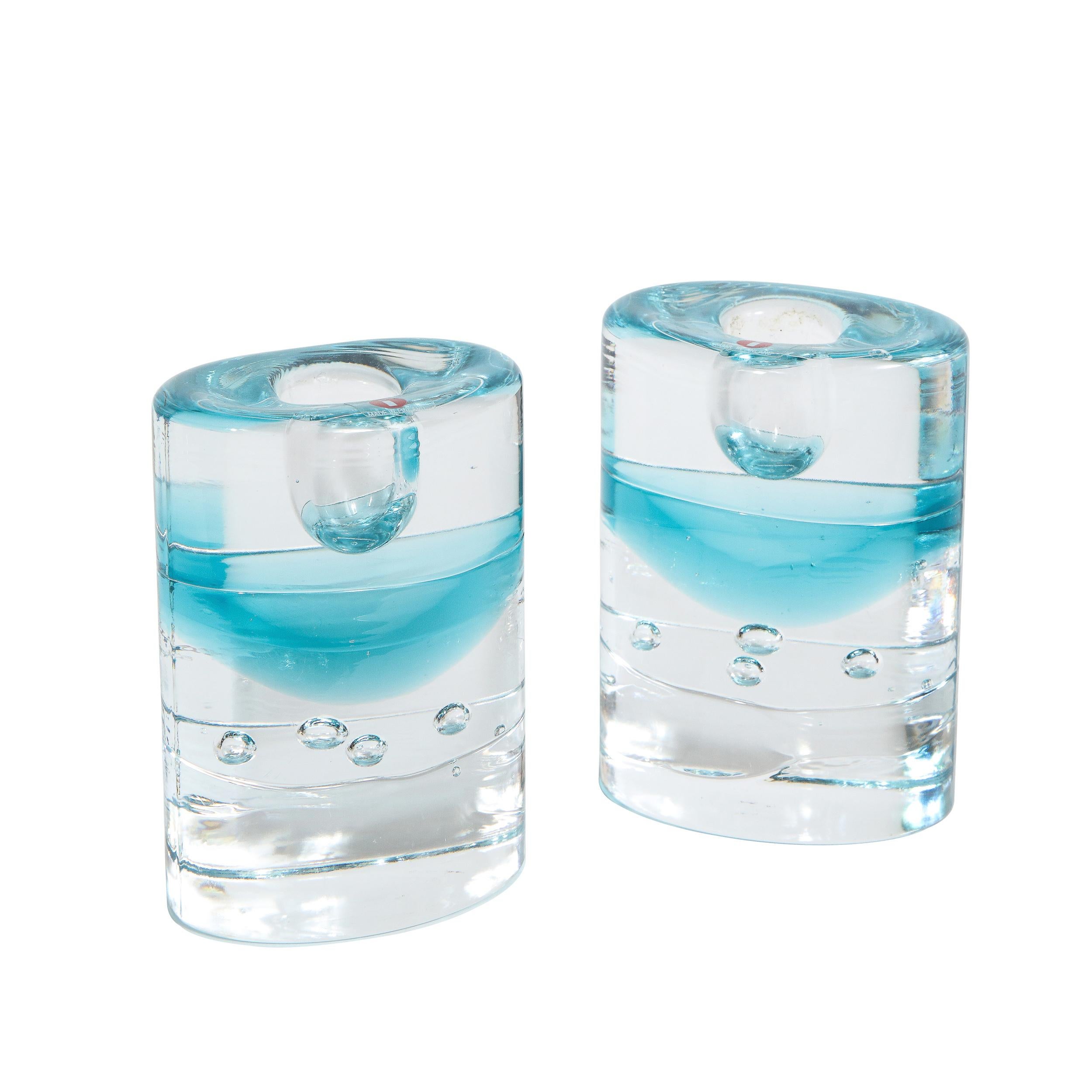 This elegant pair of candlesticks were realized by the esteemed design firm Littala in Finland. They feature volumetric elliptic bodies in translucent glass with acquamarine glass infused as a layer and clear murines resembling bubbles of water.