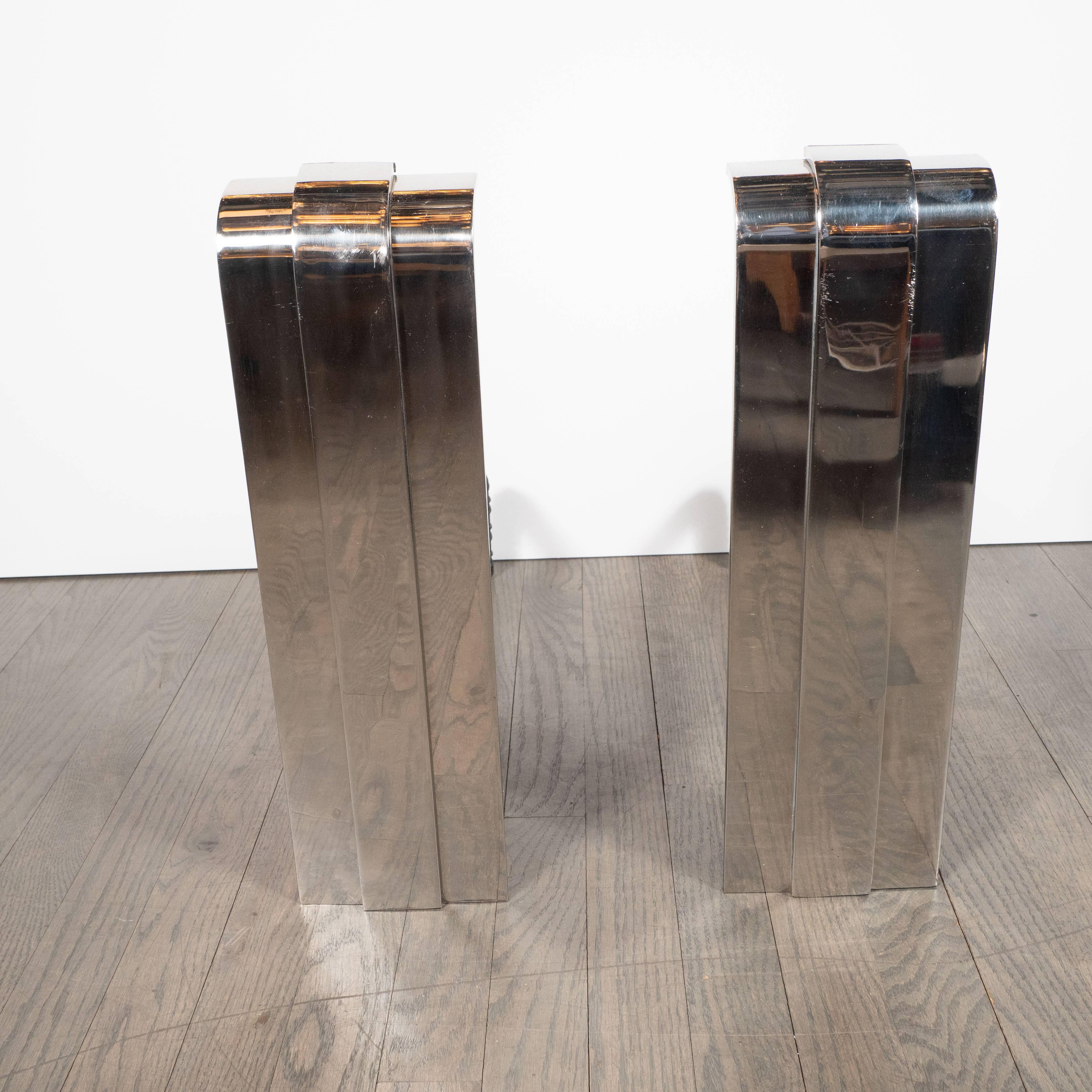 Handmade by artisans in New York state, this pair of modernist andirons embody the old world craftsmanship and design aesthetic of a bygone era. With their skyscraper style construction, they consist of three polished nickel bands, of which the