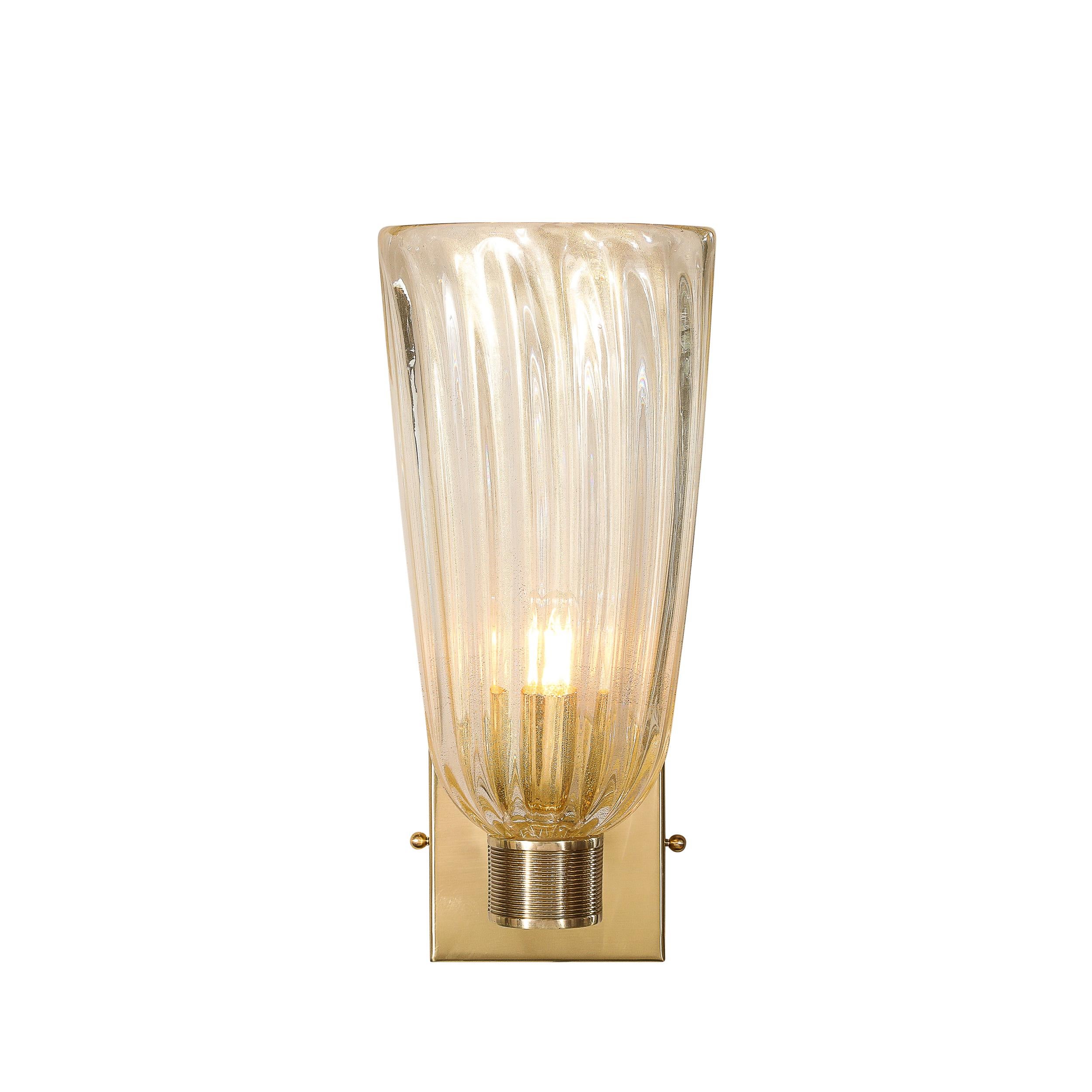 This glamorous Pair of Modernist Transparent Hand-Blown Murano Fluted Glass Sconces W/ 24kt Gold Flecks originates from Italy during the 21st Century. They feature a fluted shade rendered in transparent glass with 24kt Gold Flecks carefully