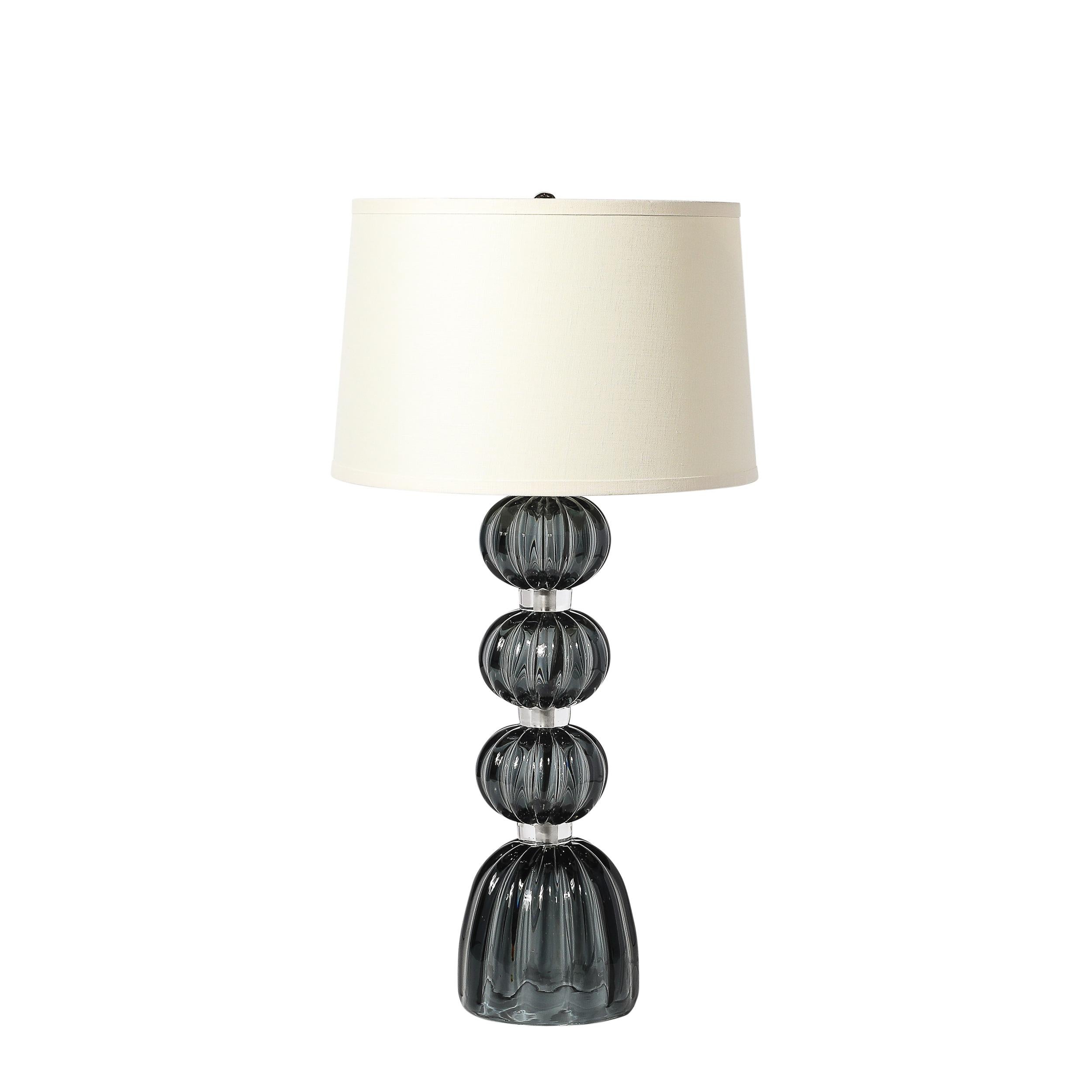 Questa coppia di lampade da tavolo moderniste esemplifica la maestria artigianale e la raffinatezza senza tempo del vetro di Murano. Ogni lampada presenta un corpo in una ricca tonalità di grafite affumicata, realizzato in una forma impilata con