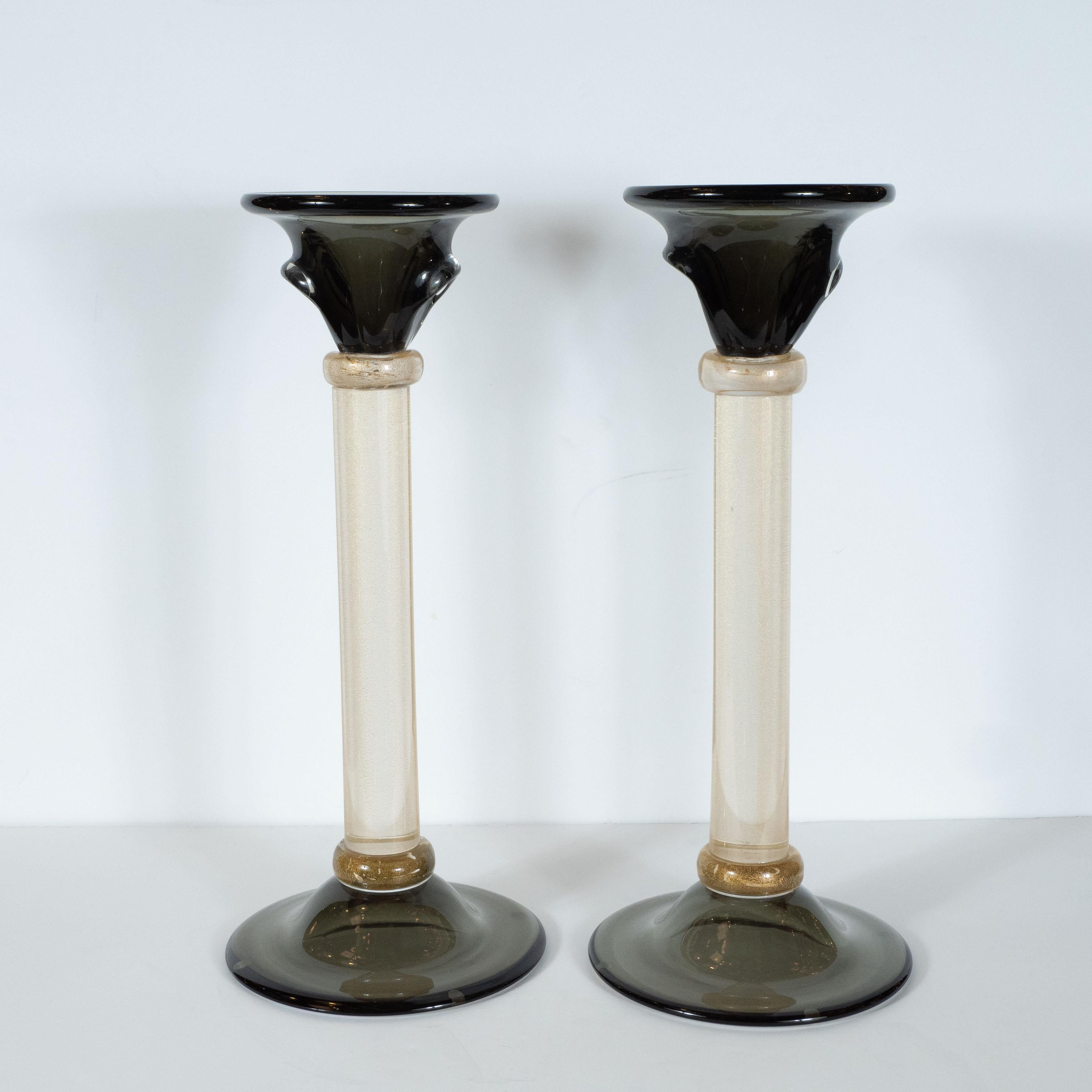 This stunning pair of candlesticks were realized in Murano, Italy- the island off the coast of Venice renowned for centuries for its superlative glass production. They feature subtly domed bases and urn form tops- with indented handles on each side-