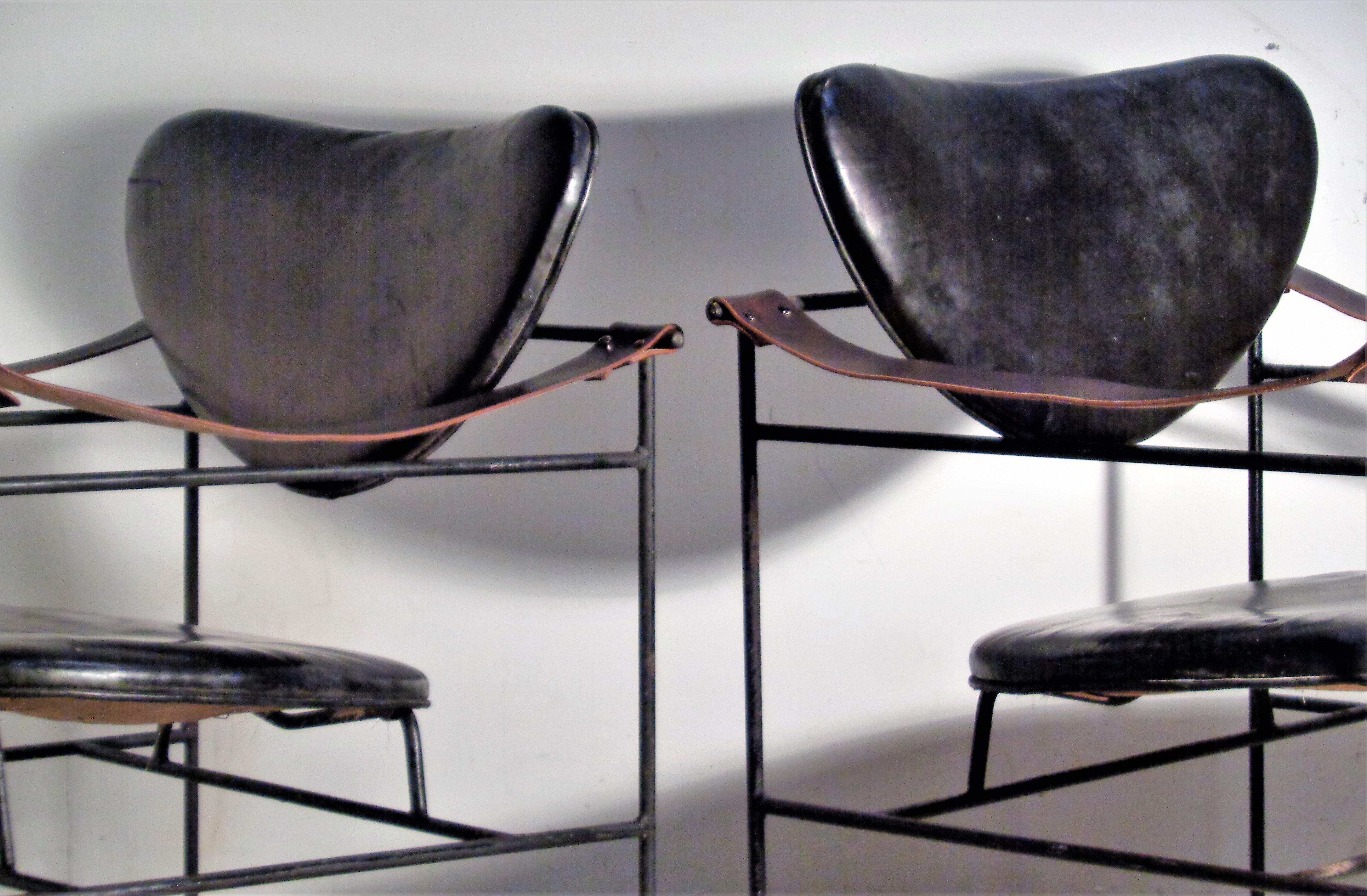 Pair of blackened iron frame lounge chairs with black leather seats and backs / brown saddle leather sling arms ( 25