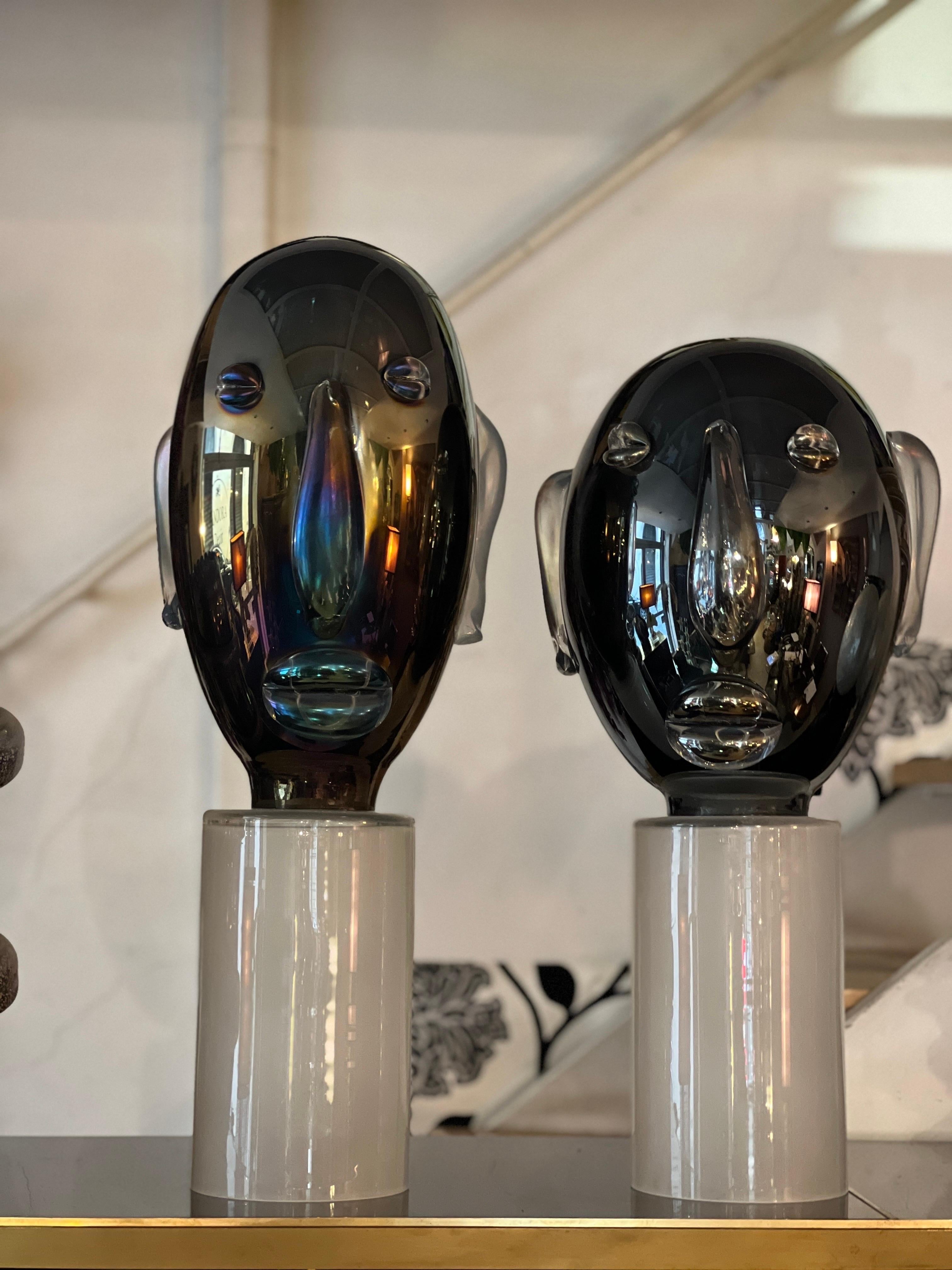Pair of Modernist Murano glass sculptures head-shaped Picasso style on clear frosted glass round base. The elongated head is made of black mirrored and iridescent Murano Glass. The applications (mouth, ears, nose and eyes) are made of handblown