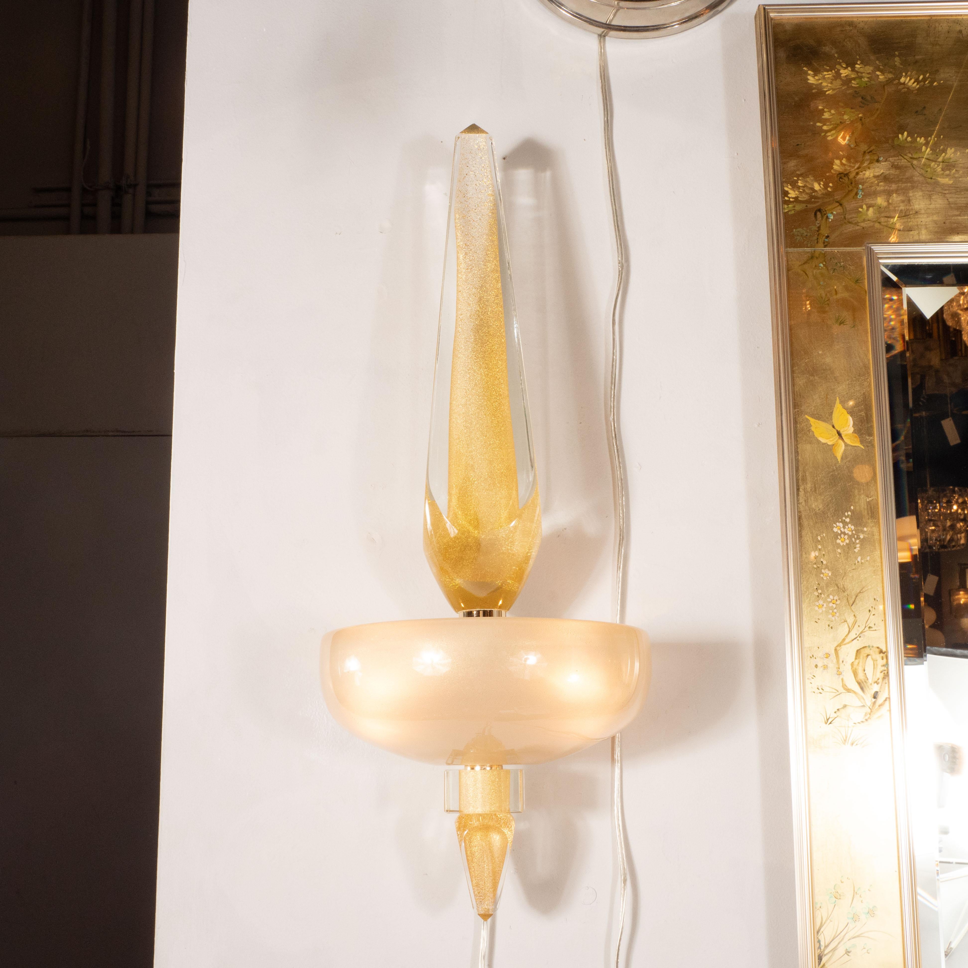 This stunning and graphic pair of sconces were realized in Murano, Italy- the island off the coast of Venice renowned for centuries for its superlative glass production. It features an obelisk form in faceted translucent glass with a shimmering