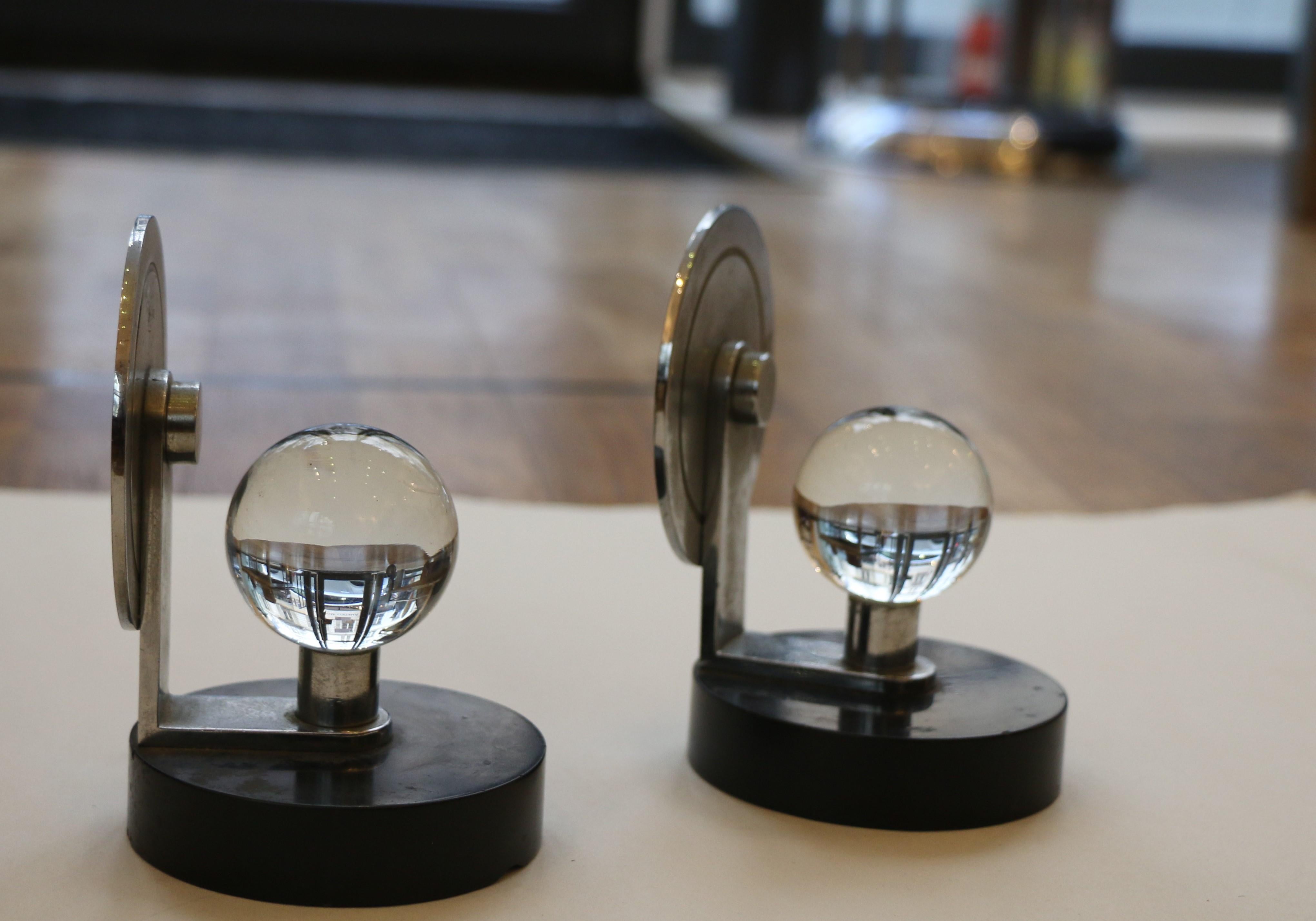 Pair of modernist paperweights functioning as bookends, made of nickel-plated metal with a black marble base and adorned with a translucent glass sphere.  
Dimensions : H : 14 cm; W: 9 cm
____________________
Paire de presse papiers formant serre