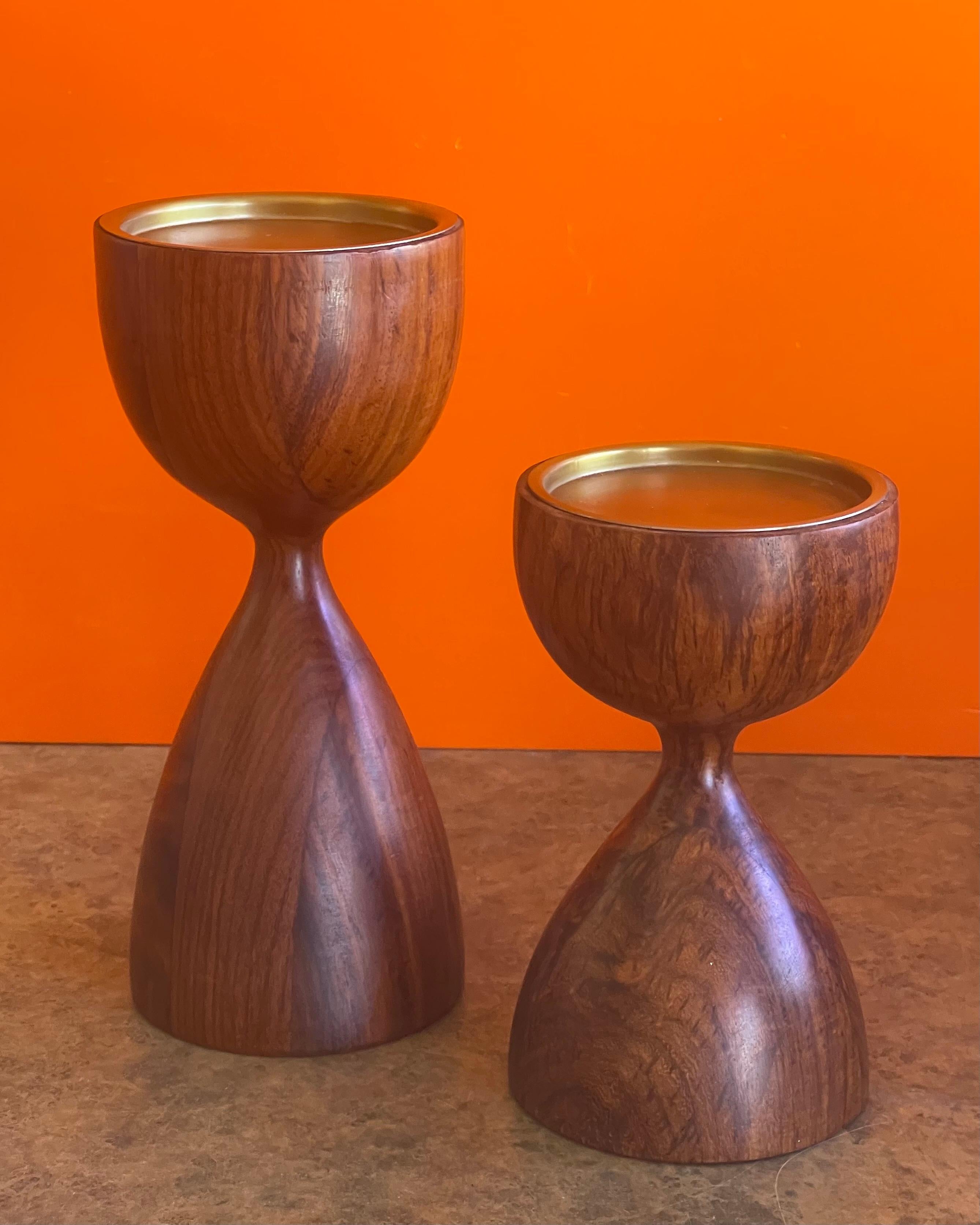 Pair of modernist rosewood candlesticks, circa 1970s. The pair are in very good condition and are capped with a round brass candle liner. The diameter of the holders are 3.75