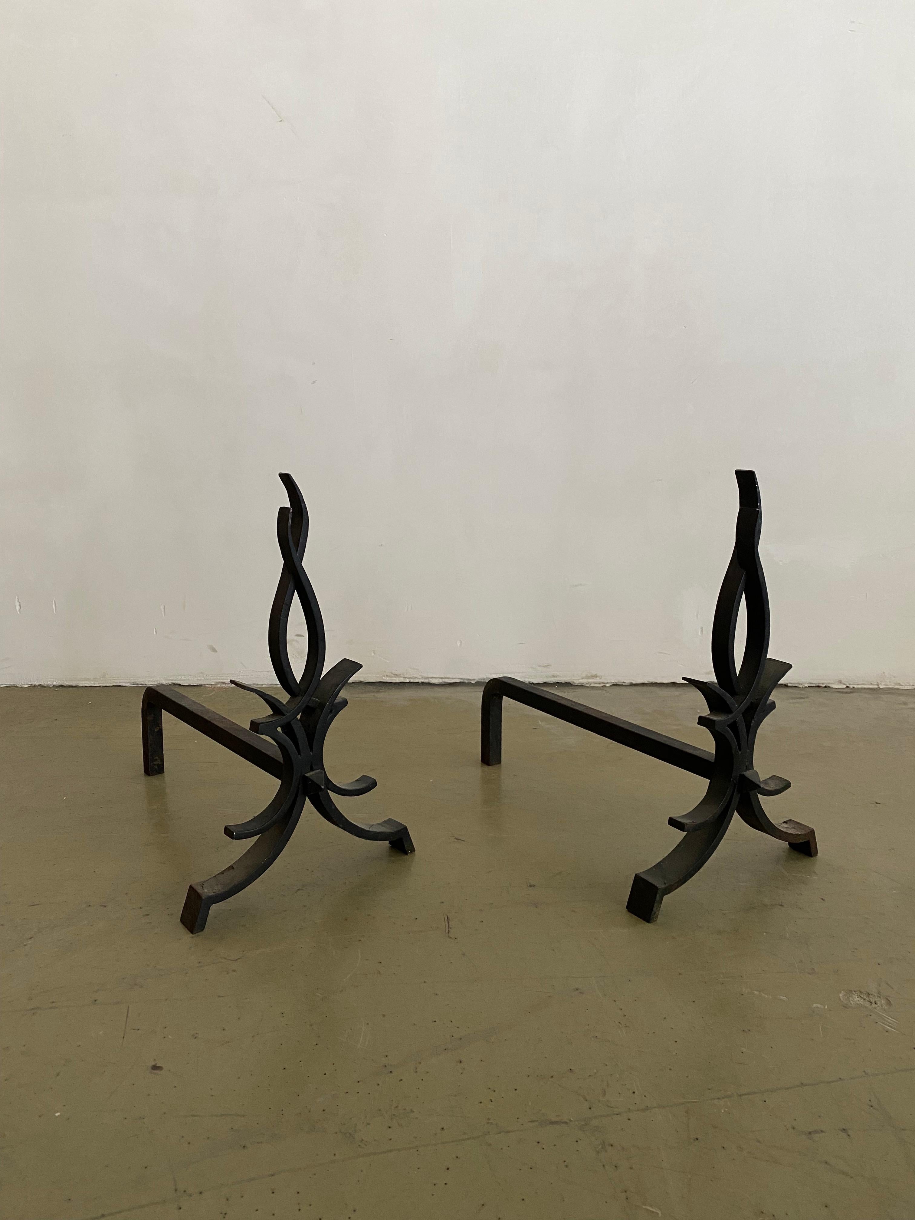 Pair of wrought iron andirons with a minimalistic representation of the fire it holds.