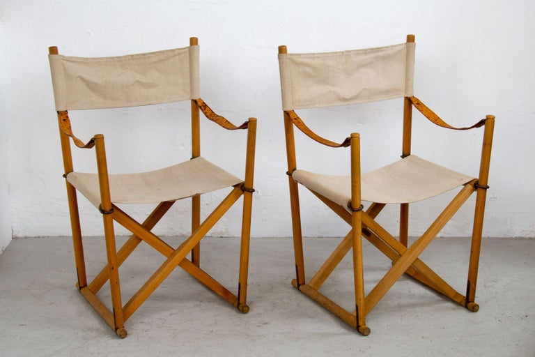 Pair of folding chairs designed by Mogens Koch in 1932 and manufactured by Interna Denmark cabinetmaker. Made in natural beech wood and brass. Back, seat and cushions in light canvas. Armrests in full grain leather. Included brass plaquette signed