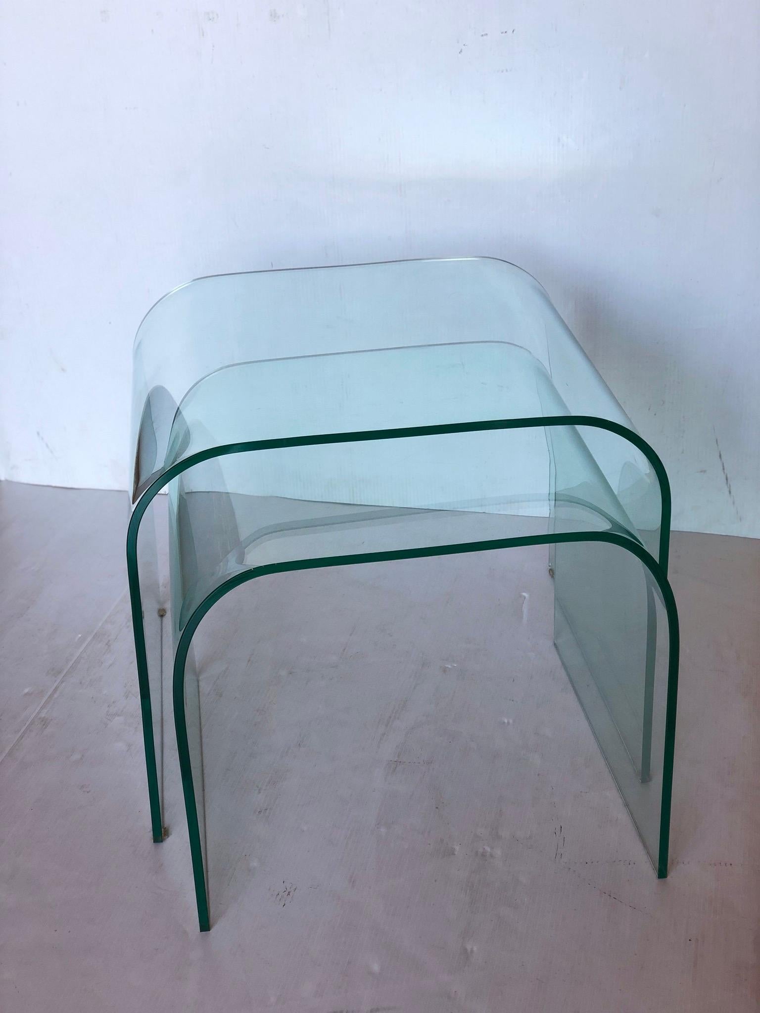 Minimalist pair of Italian molded glass nesting or drinks tables designed by Angelo Cortesi for Fiam Italia. Each has a modern waterfall design made of bent crystal glass and each is signed on the corner by Cortesi. Beautifully constructed, also