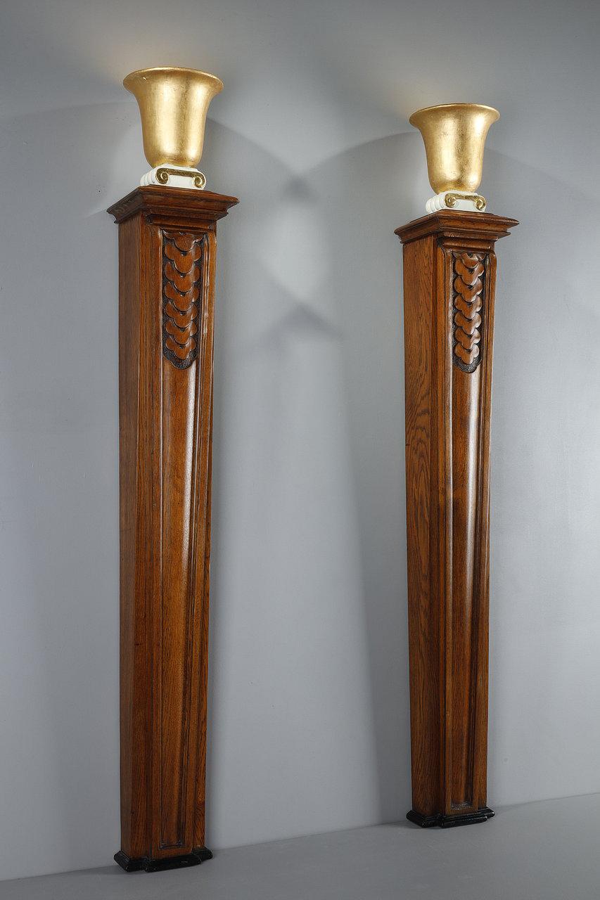Important pair of Art Deco style columns in molded oak, each surmounted by a Medici vase in gilded gesso with gold leaf, forming a lamp. These large Art Deco columns to be fixed to the wall, are decorated in the upper part of a frieze of tri-lobed