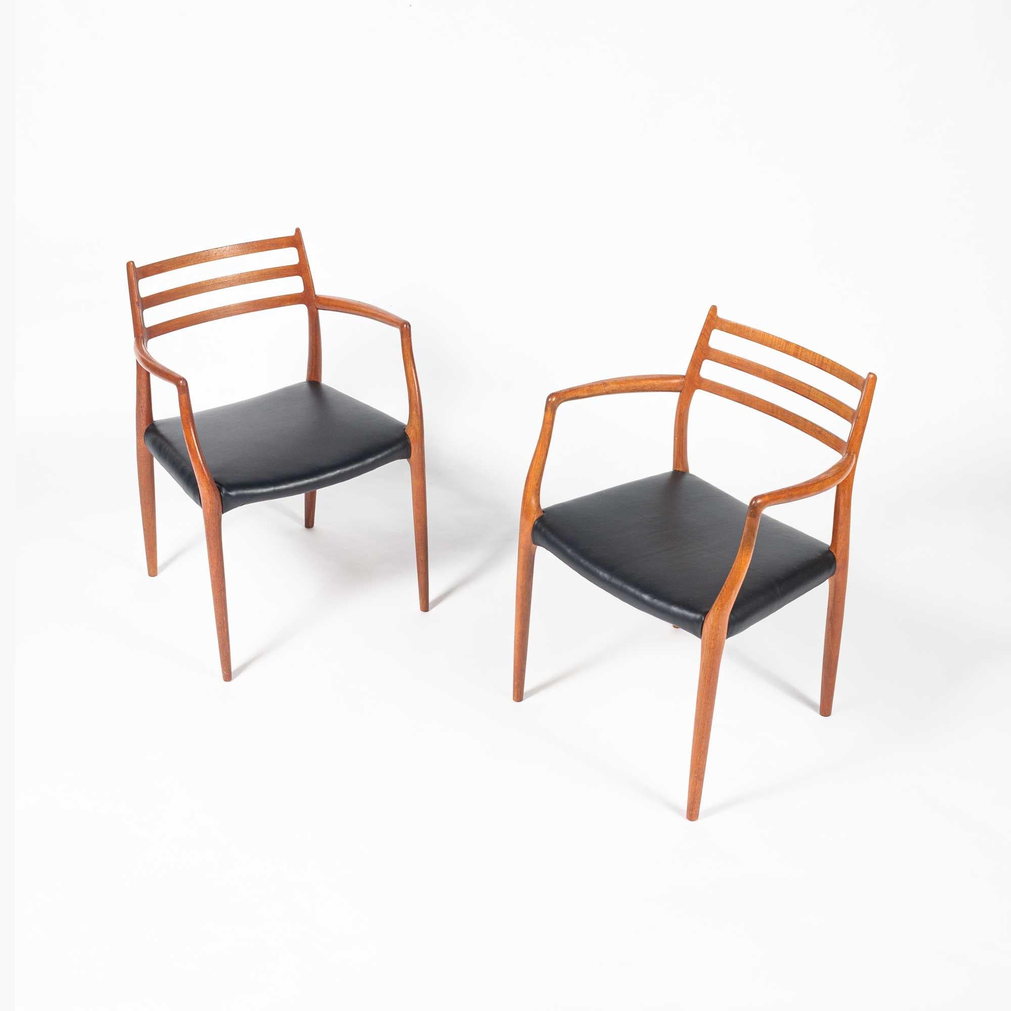 Iconic pair of teak dining/captain chairs designed by Niels Otto Moller for JL Møller Møbelfabrikin 1954, Moller 62. Frame is in vintage condition, with newly reupholstered black leather seats.