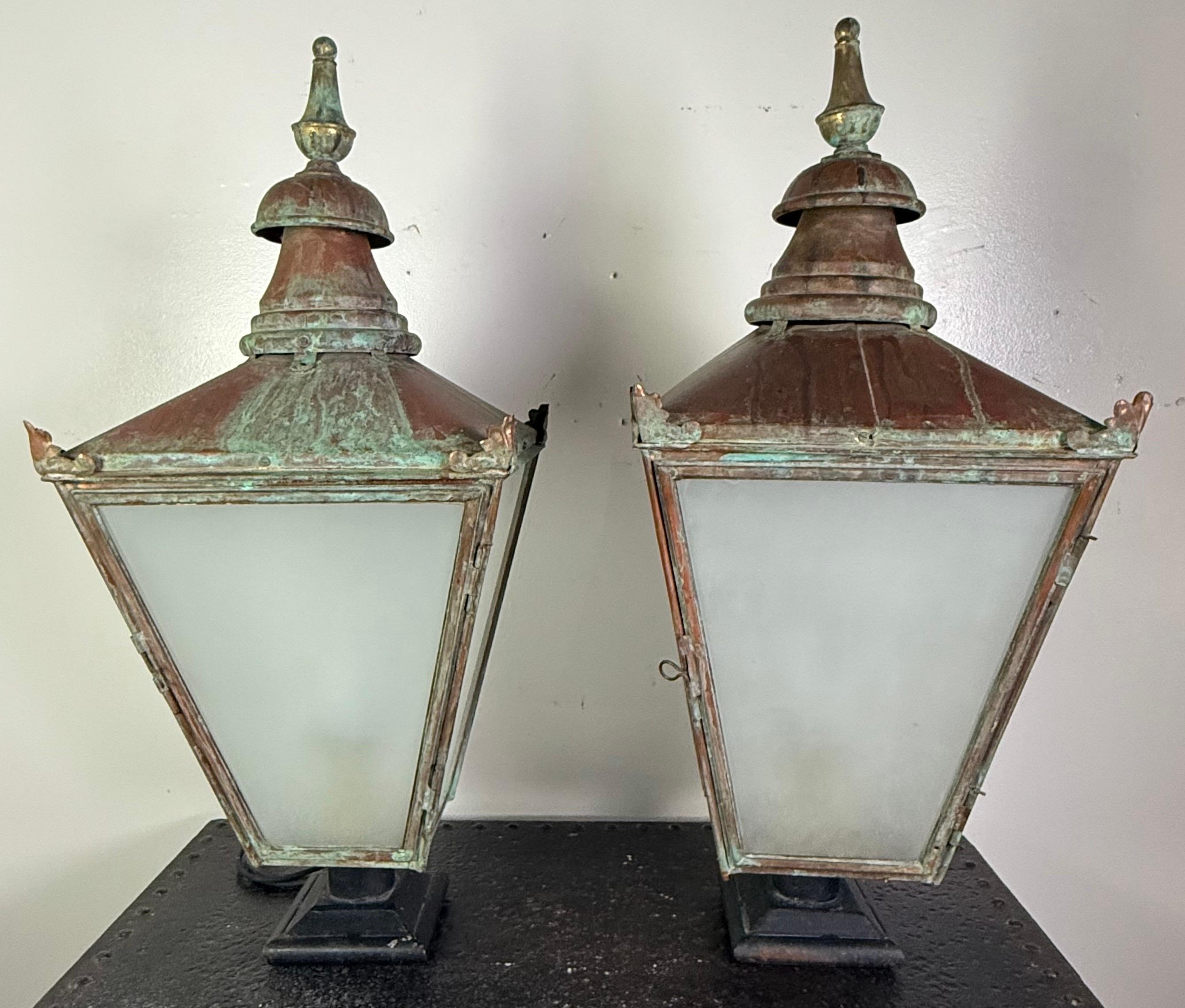 Magnifique paire de lanternes anciennes en cuivre, probablement du début du 20e siècle, provenant d'une propriété ou d'un paysage urbain. Leur conception effilée à quatre côtés est couronnée par d'élégants épis de faîtage à gradins, mettant en