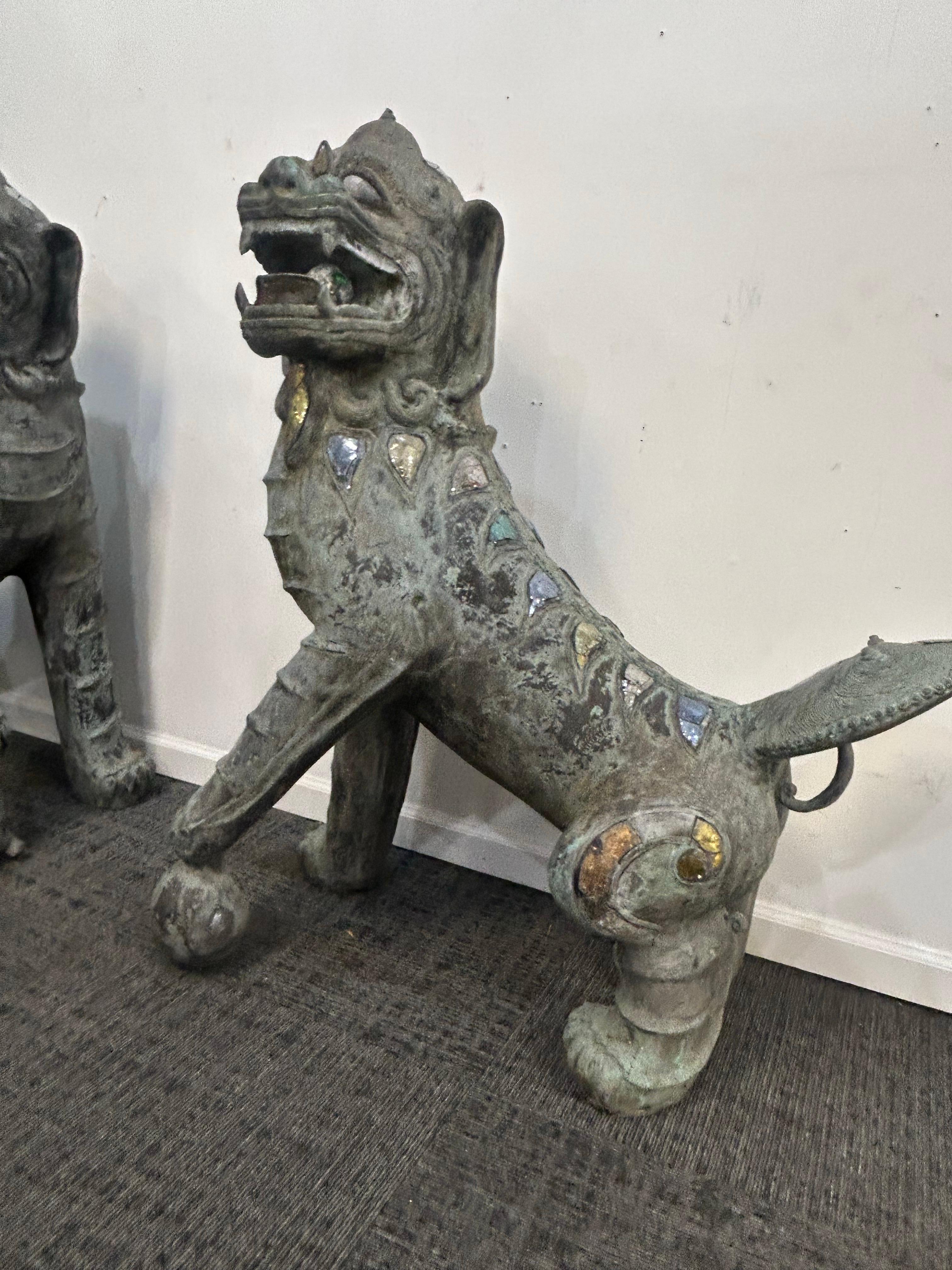 Monumental pair of opposing bronze foo dogs or guardian lions… This is a male and female pair. The male has his paw on top of the globe, and the female has her paw on top of their pup. The tails are large and fan shaped and upward, sweeping  . The