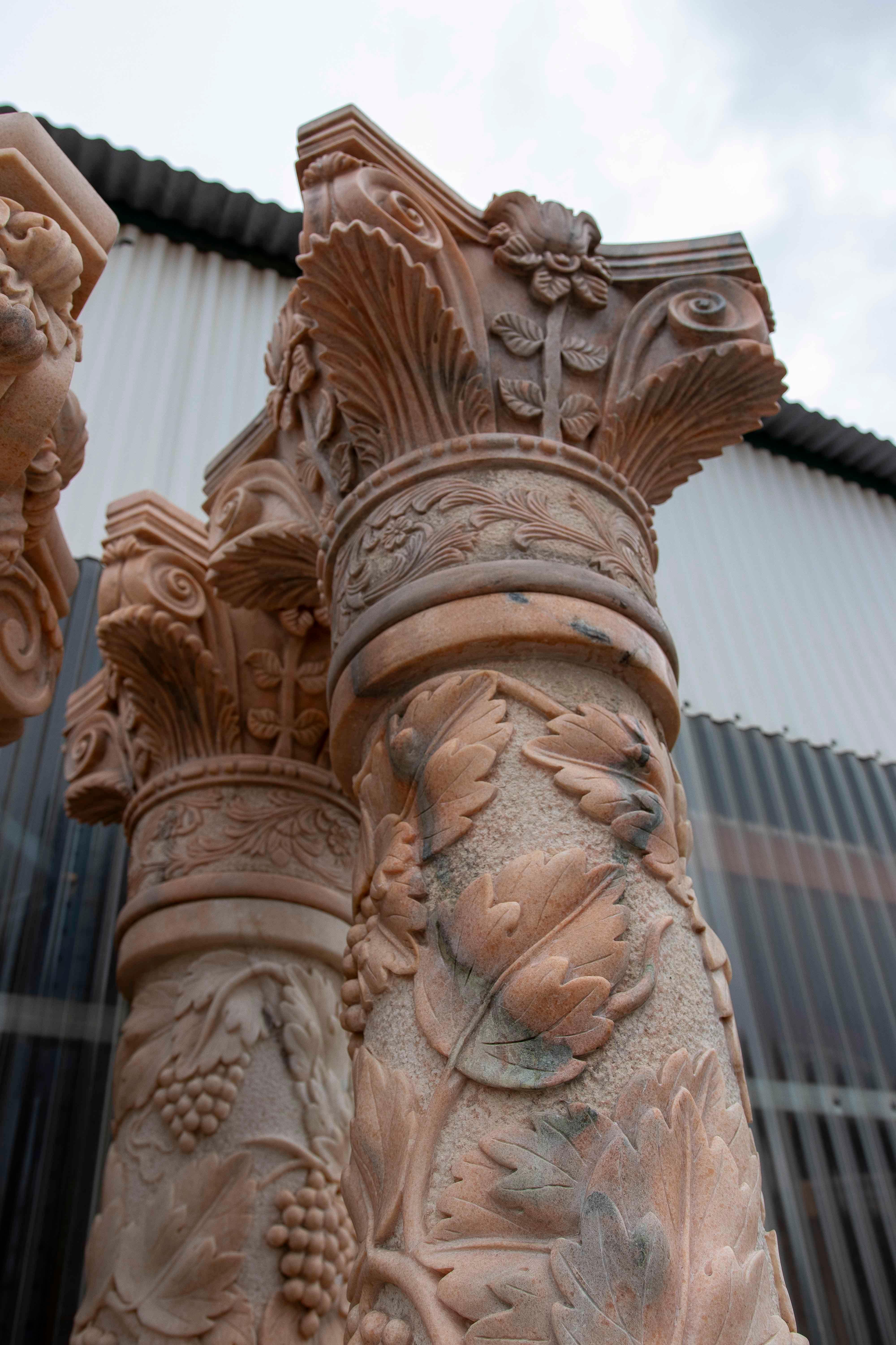 A spectacular pair of hand-carved natural marble columns with richly ornamented Corinthian capitals and shafts decorated with bunches of grapes, leaves, and other plant motifs in relief. Their design evokes classical symbolism of abundance and