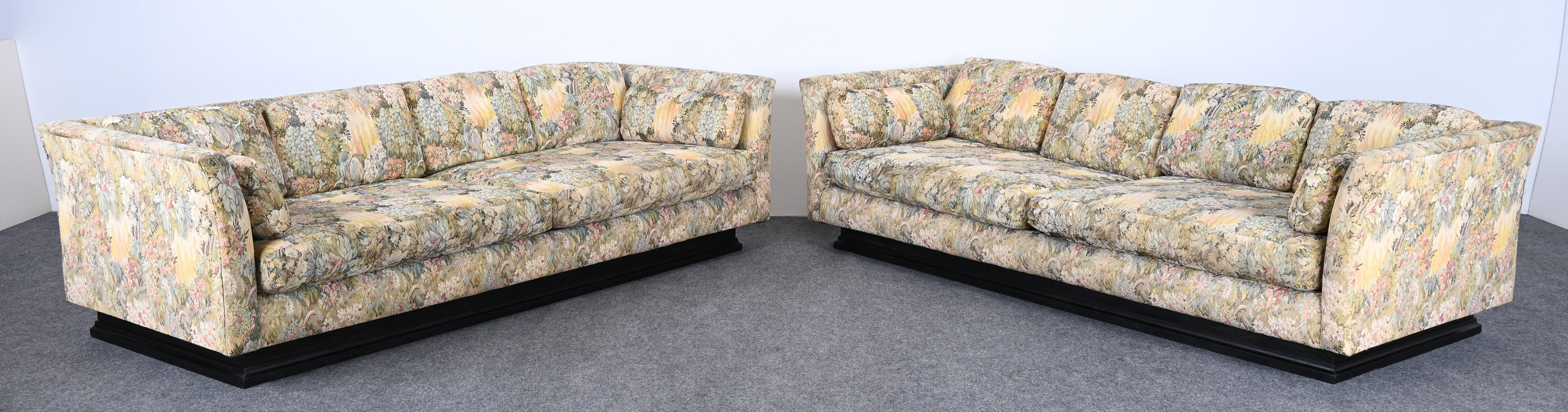 A pair of monumental tuxedo sofas on ebonized platform bases. These sofas are vintage and are in the manner of Edward Wormley, Dunbar, and James Mont. Great form to reupholster. New upholstery is necessary. These sofas would look great in any modern