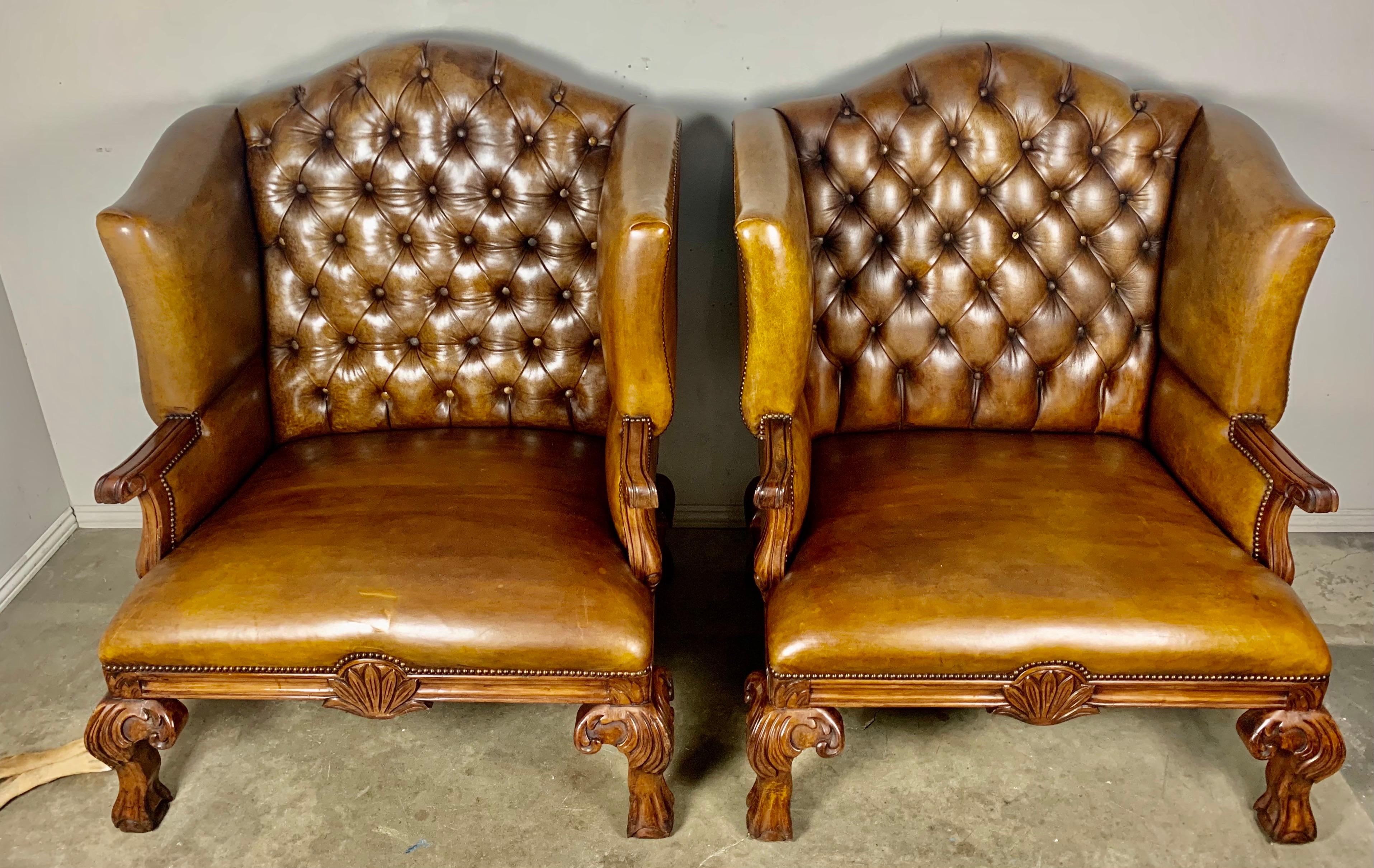 Pair of monumental English wingback leather armchairs that have tufted backs and nailhead trim detail. The chairs stand on four Queen Anne style legs with lion paw feet. The leather is in excellent condition with a slight imperfection in one of the
