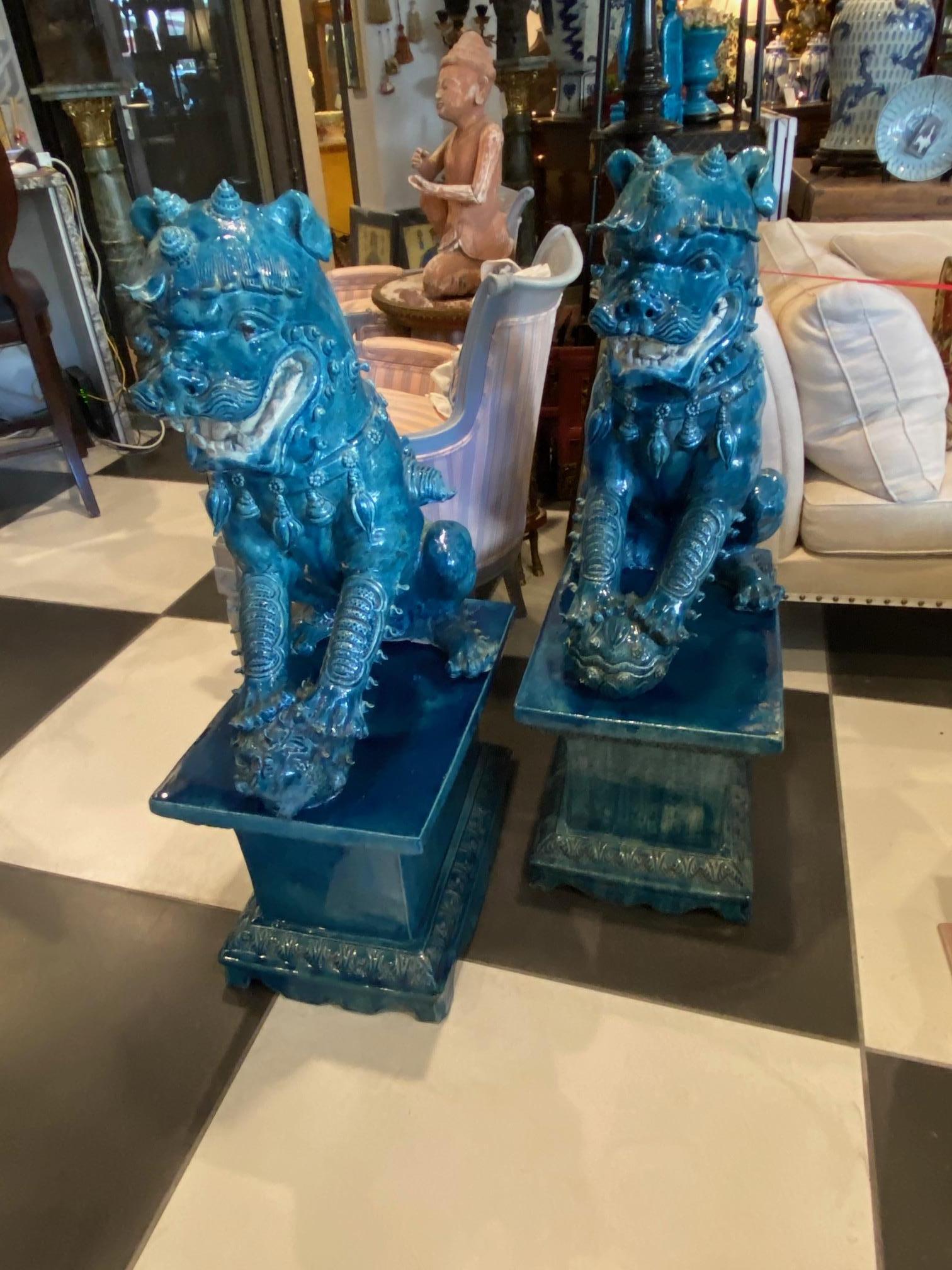 The pair of turquoise glazed monumental foo dogs on separate stands are well done month open, tongue extended, male holding the world and the female holding the baby. Tails open a lot of detail in both.