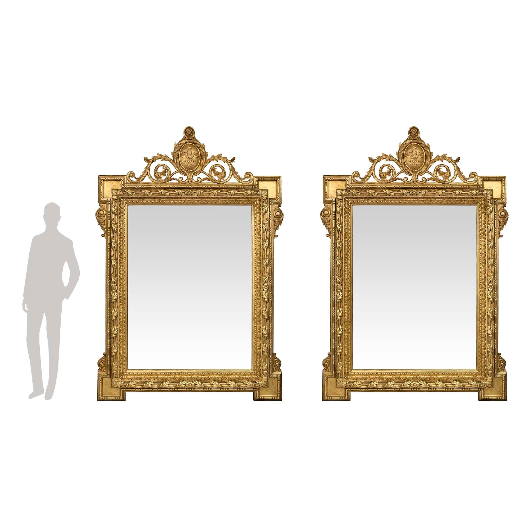 Une paire spectaculaire et monumentale de miroirs en bois doré de style Louis XVI du XIXe siècle. Chaque plaque de miroir originale est encadrée d'un remarquable motif torsadé et perlé richement sculpté. Le cadre épais et remarquable présente des