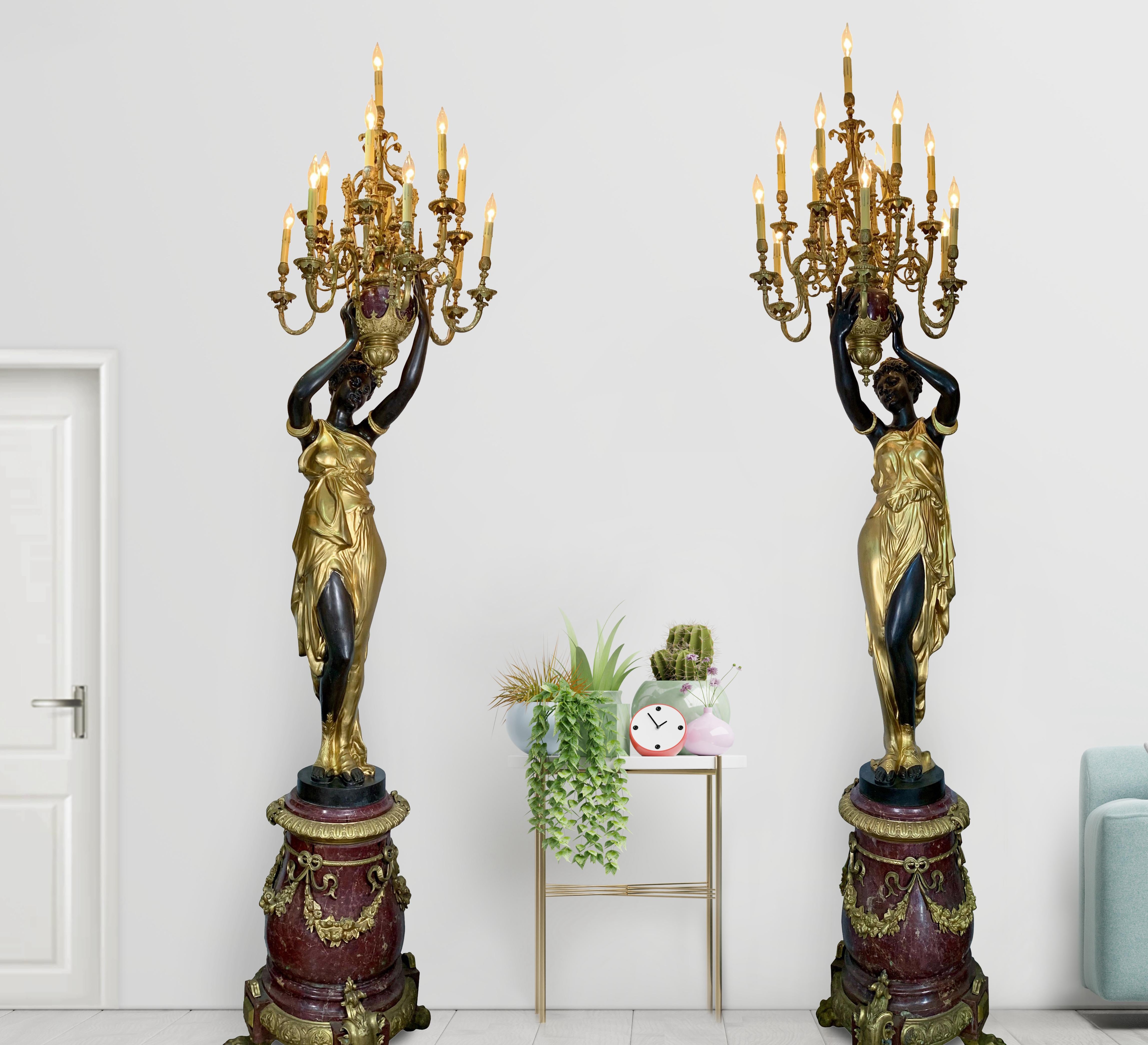 A pair of large French parcel-gilt patinated bronze and rouge marble 13-light torchieres after the models by Albert-Ernest Carrier-Belleuse (1824-1887).  Each torchere modeled as a classically-draped maiden holding aloft an urn issuing scrolling