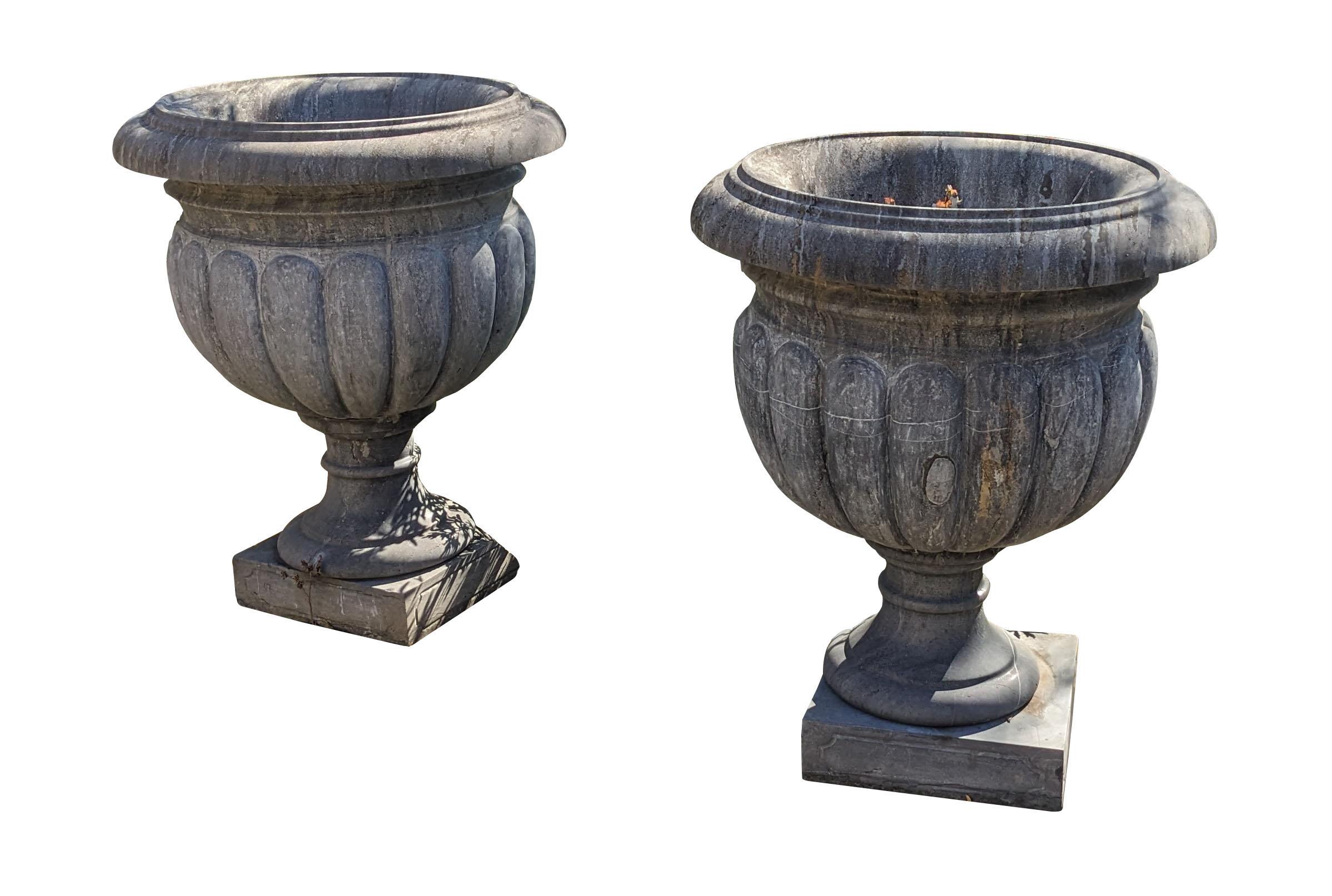 Large pair of stone Grecian style urns on stand.  Features a large opening for plants or small trees over a gadrooned exterior leading to a base over plinth.  A great set to flank a doorway or entryway.

Dimensions:
32