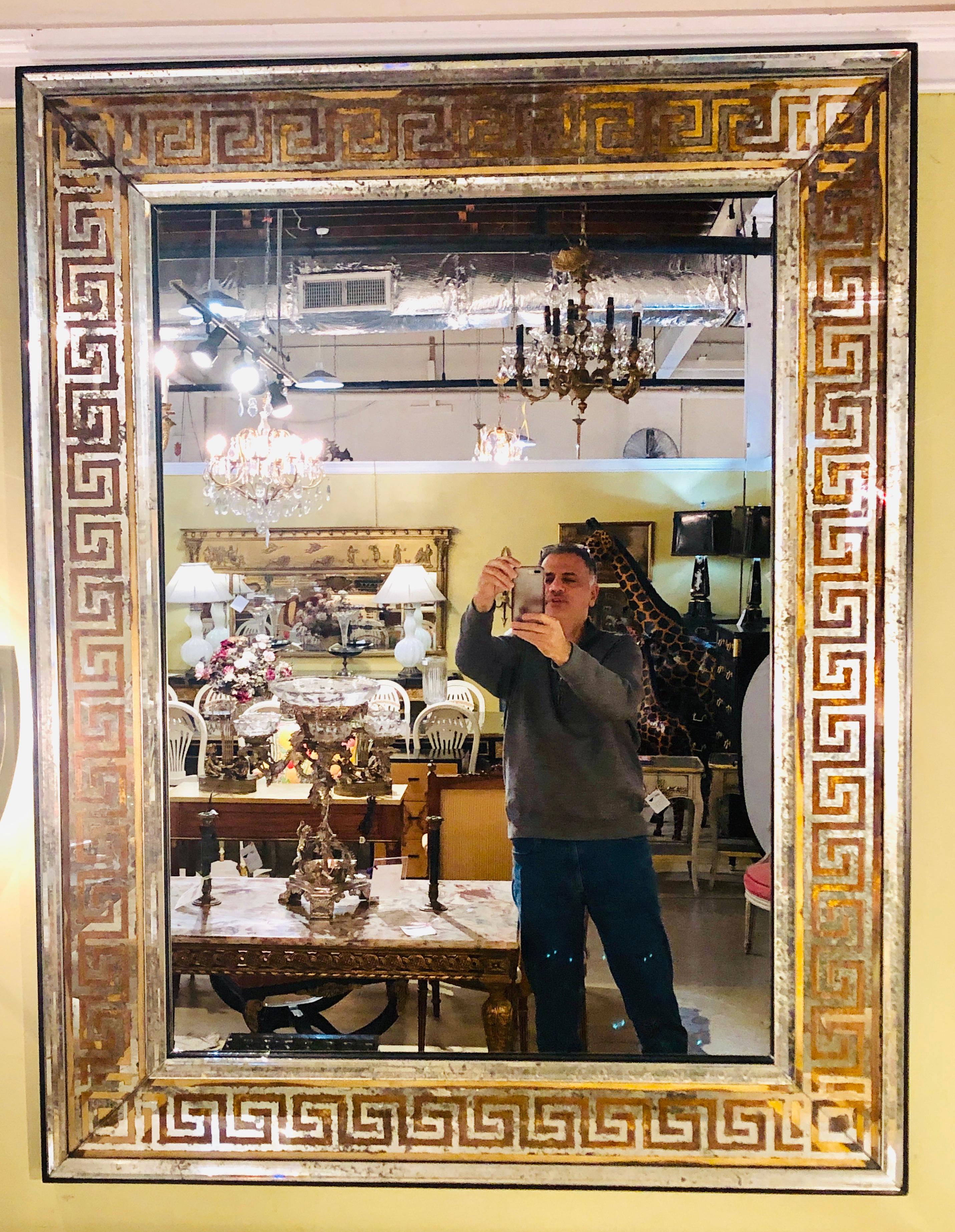 A fine pair of custom quality Hollywood Regency style etched gilt gold and silver leaf insert Greek key wall or console mirrors. The clean and clear center mirror having a distressed antiqued thin beveled frame which flanks a etched Greek Key design