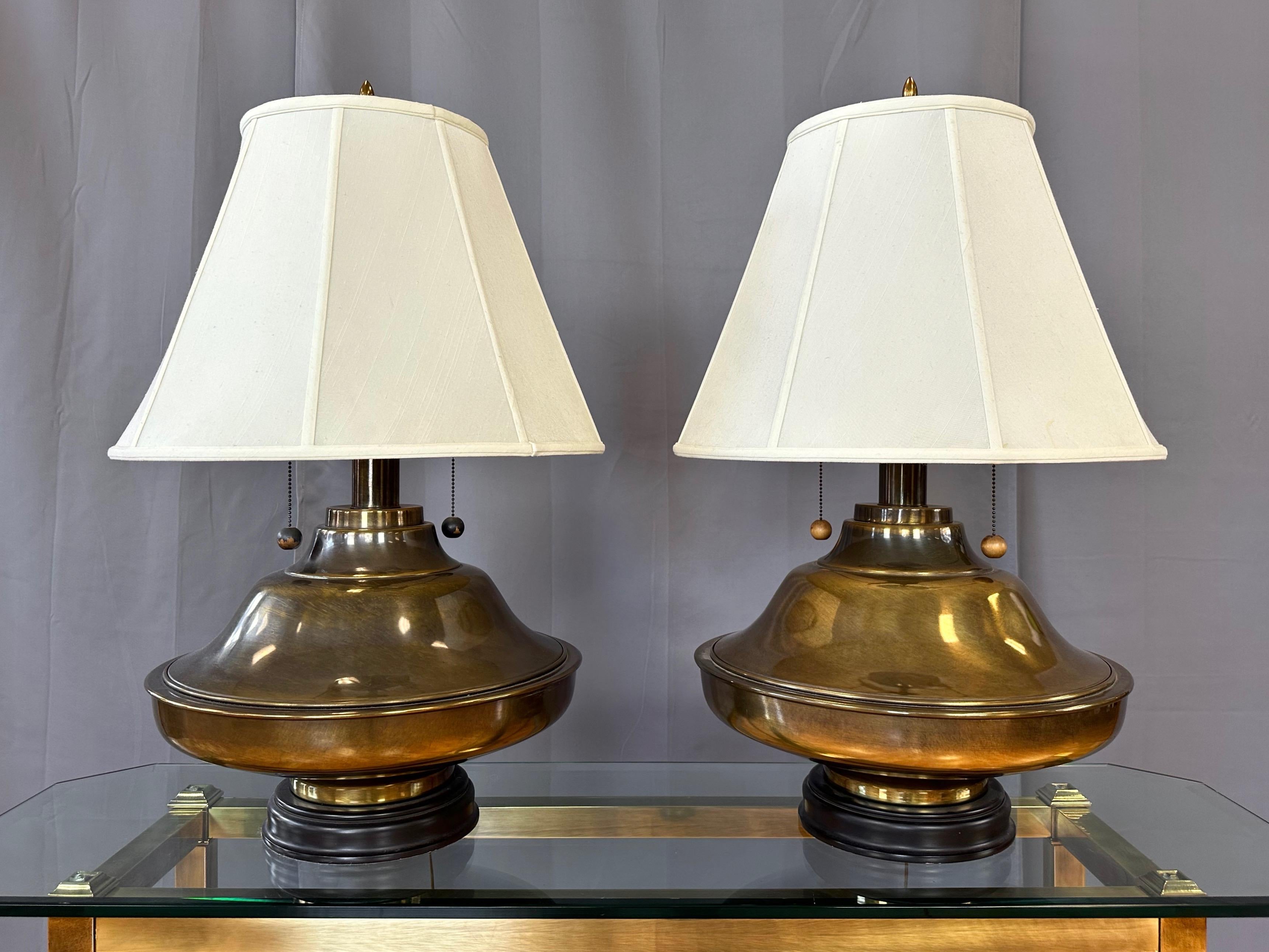 A pair of monumental 1960s Marbro-style Hollywood Regency antiqued brass table lamps with silk shades.

Very substantial and visual striking round brass bodies feature a quite uncommon form not seen in other lamps produced by the same manufacturer
