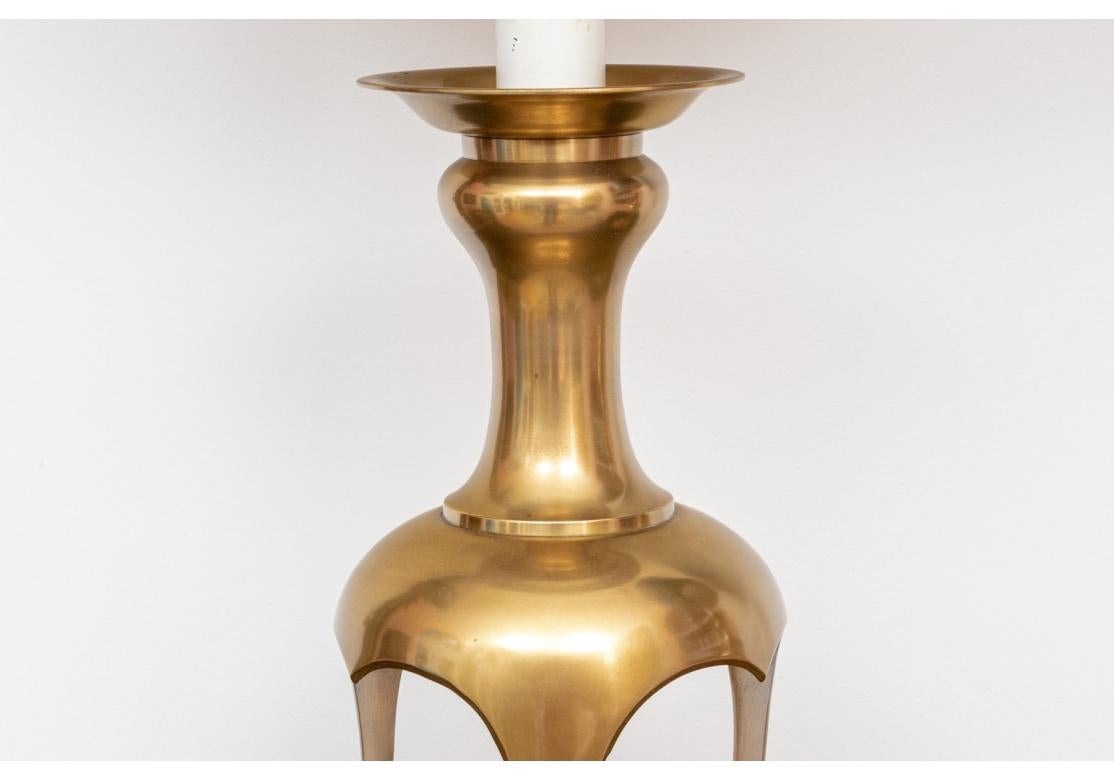 Pareja de lámparas de latón de mediados de siglo con grueso candelabro, base calada y apoyada sobre patas trípodes, rematadas en un zócalo redondo de metal negro al estilo de James Mont. Las lámparas con doble casquillo y funcionamiento por cadena