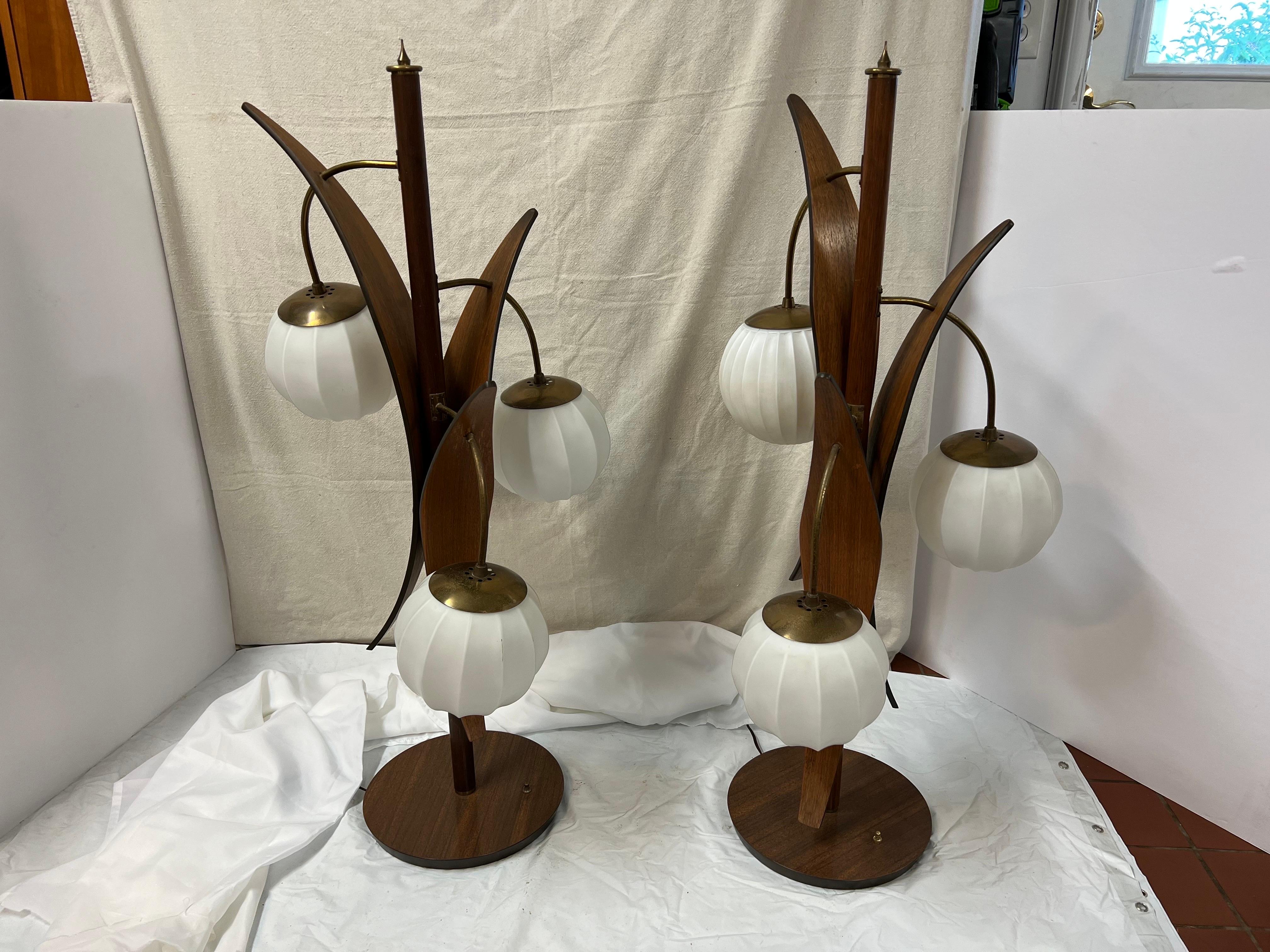 Monumental Pair of Teak Floral table lamps. These are quite the statement piece. Three globes each lamp. Three way switch on each lamp. One globe does not match the other original ones and has been replaced. It has a hairline crack in it but can be